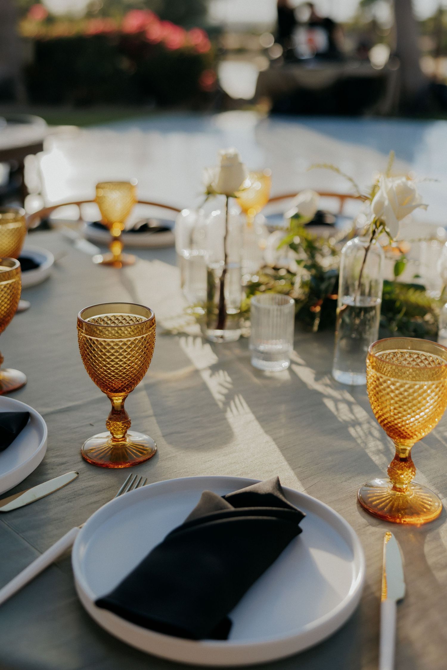 Elegant table settings with amber-colored vintage goblets and white plates against black napkins at a wedding reception.