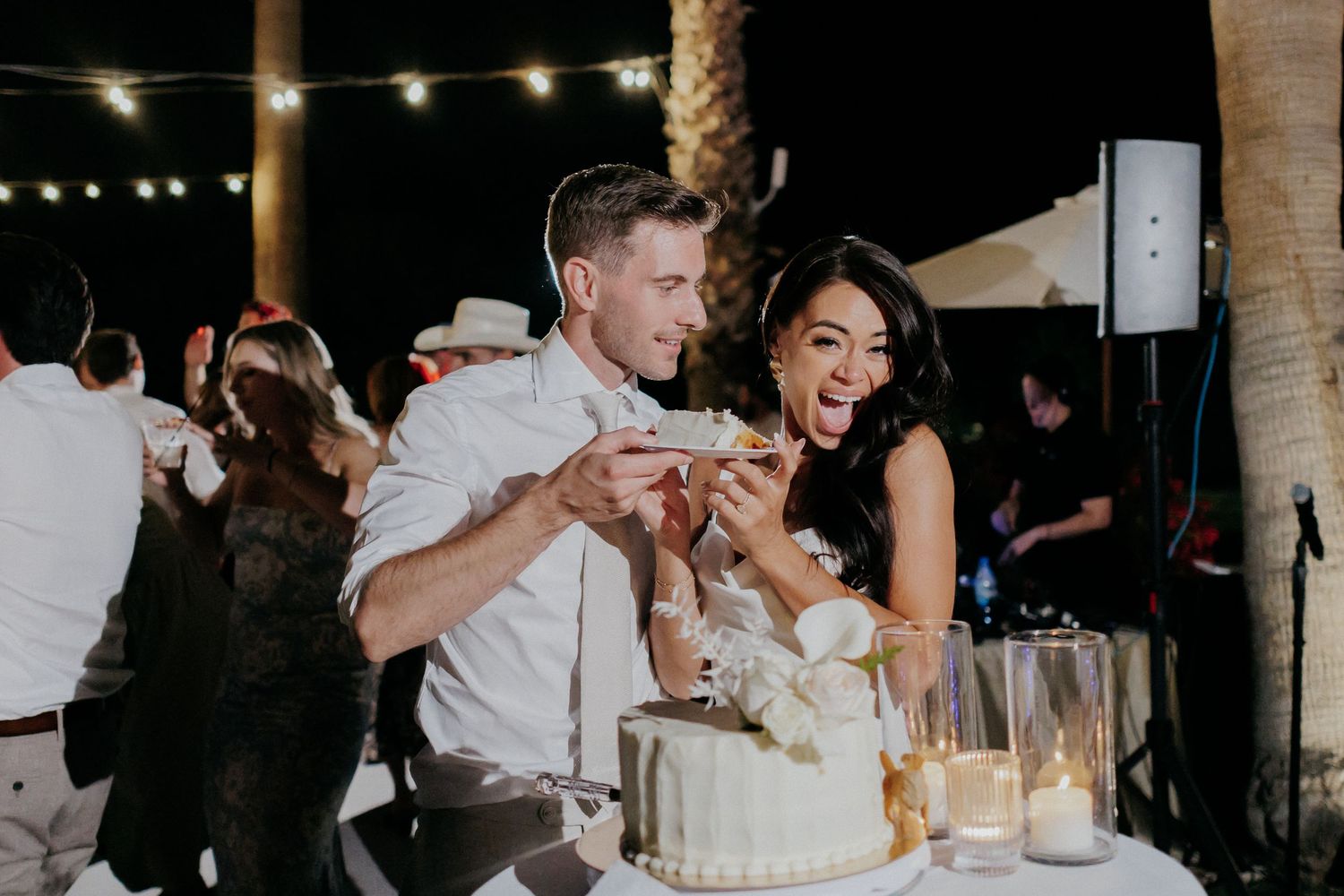 Wedding guests dancing and celebrating under string lights at an indoor reception venue during evening festivities.