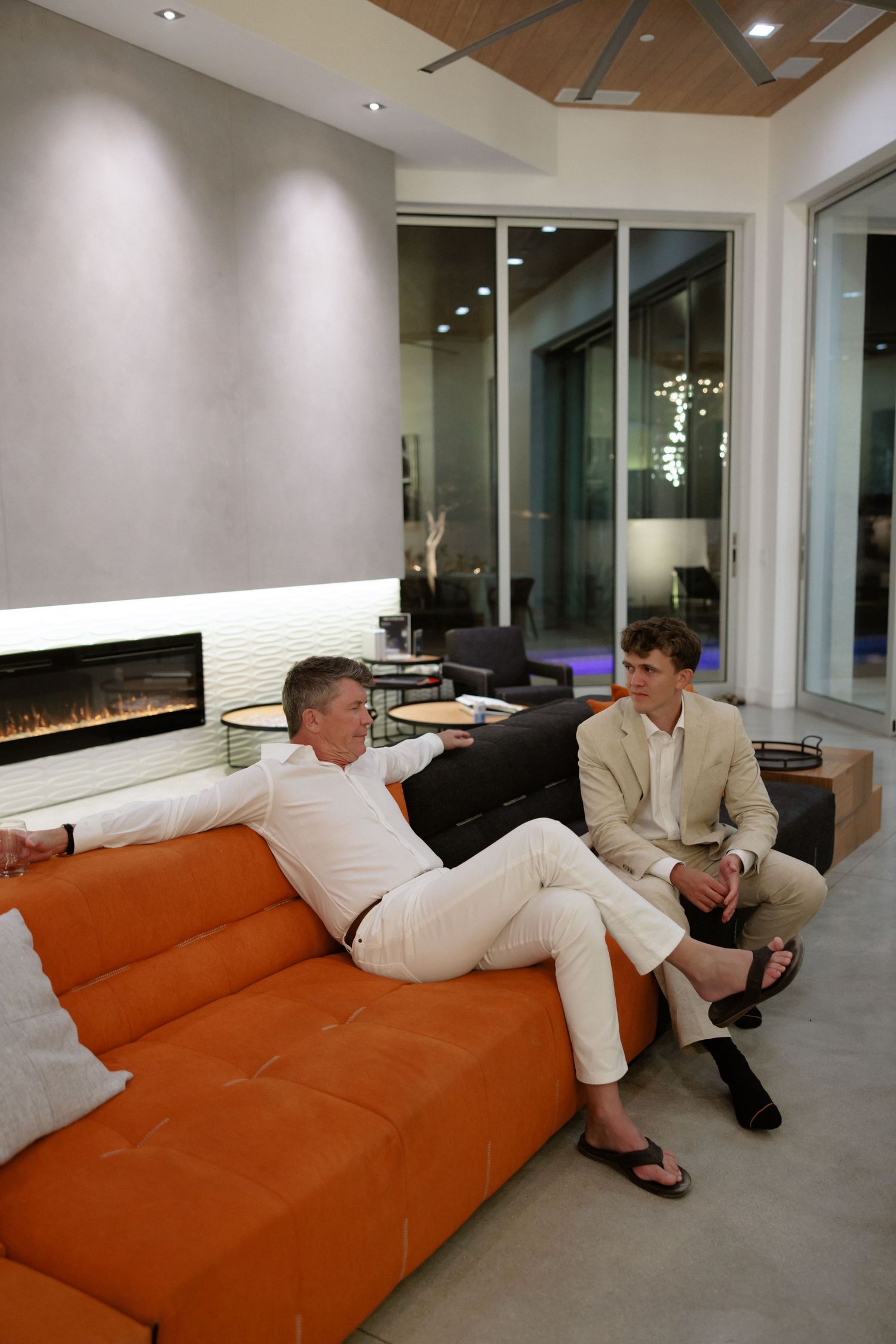 People relaxing on a modern orange sectional sofa in a contemporary living room with recessed lighting.