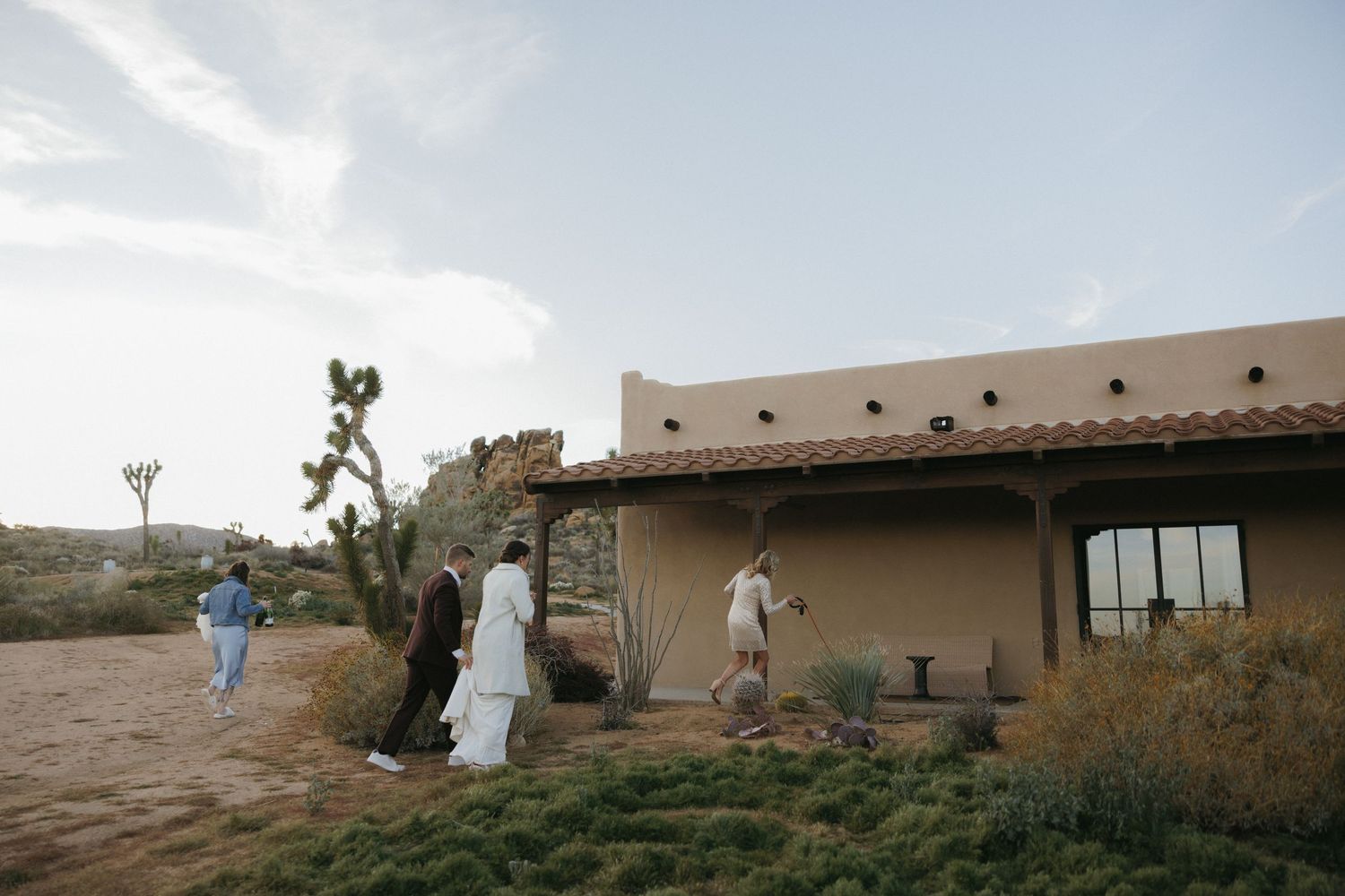 Wedding guests arrive at rustic adobe venue surrounded by desert landscape.