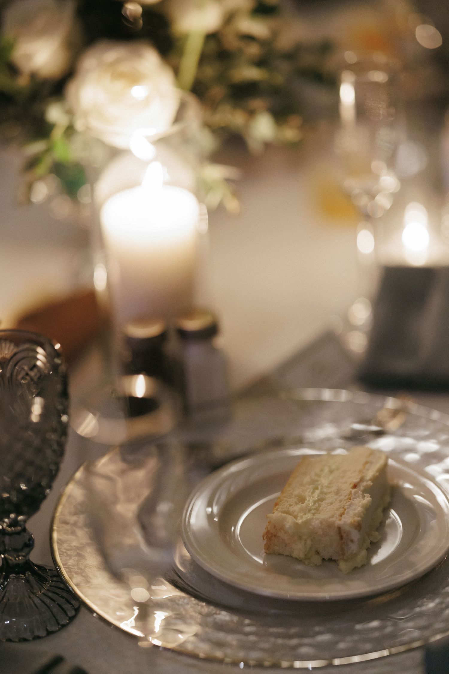 Elegant wedding reception table with white roses, candles, and slice of wedding cake.