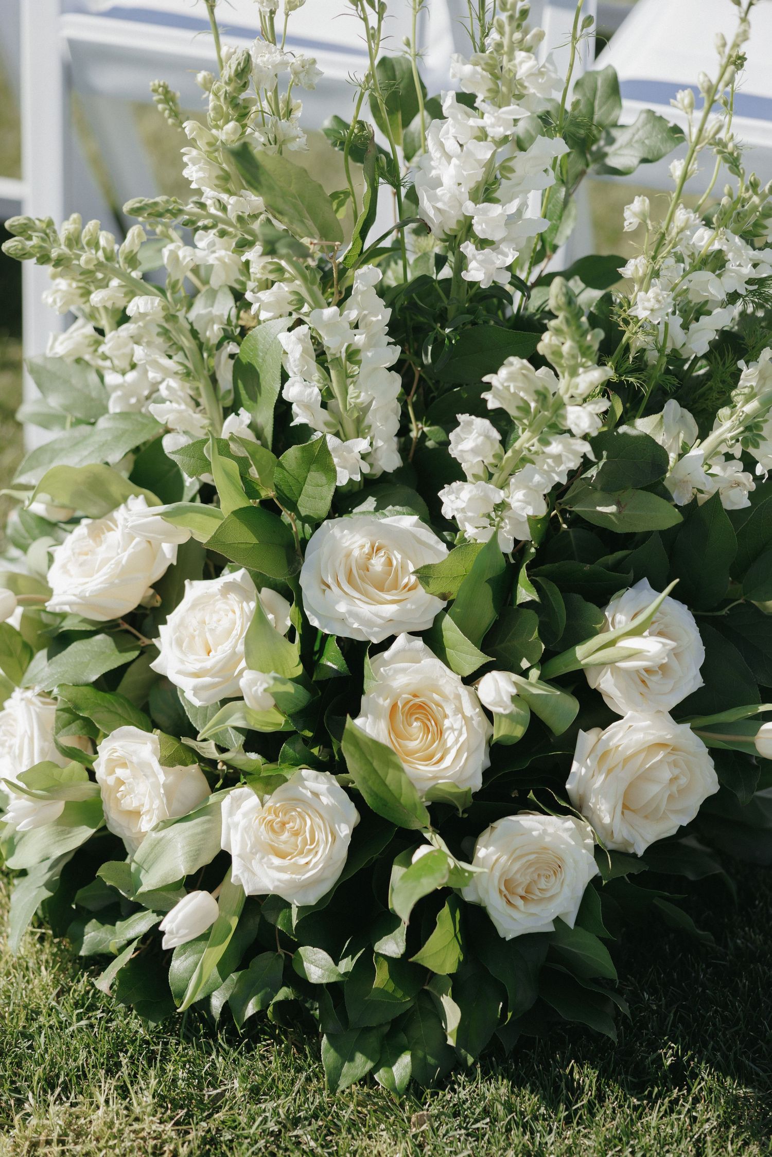 Beautiful white rose and snapdragon wedding ceremony floral arrangement on green grass.
