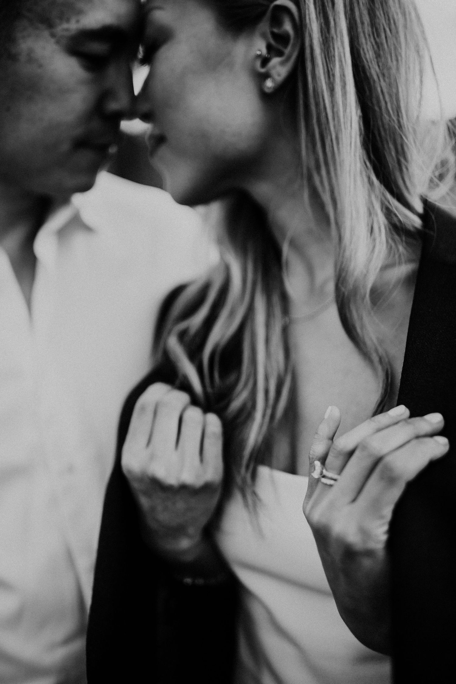 Romantic black and white close-up photo showing an intimate couple nearly kissing with an engagement ring visible.