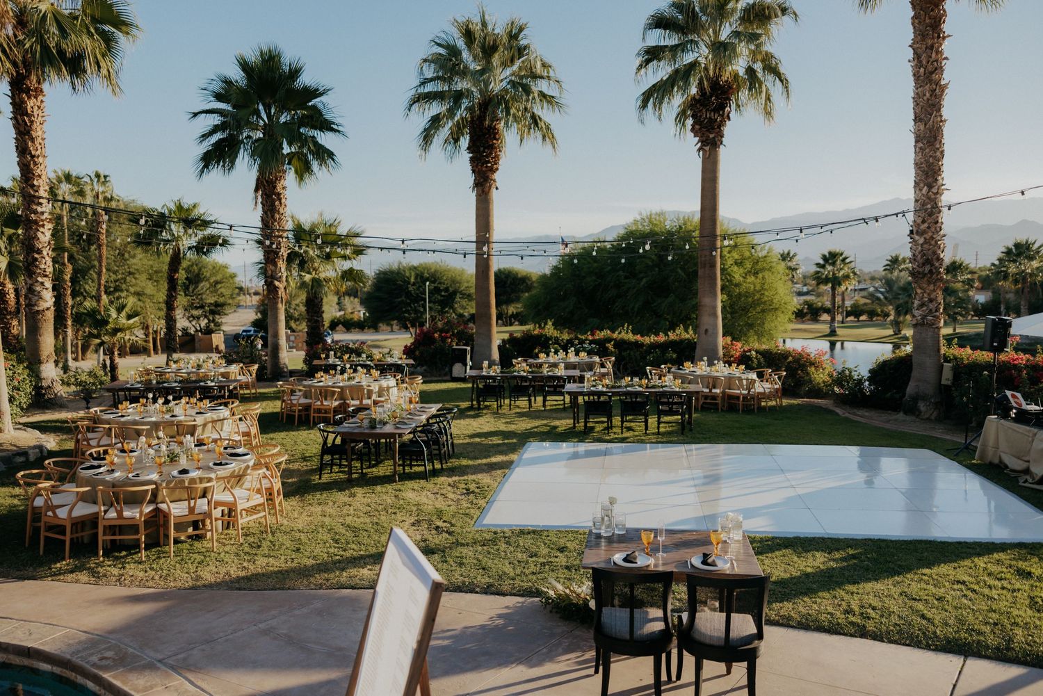 Tropical resort patio overlooking a marina with palm trees and outdoor dining furniture at sunset.