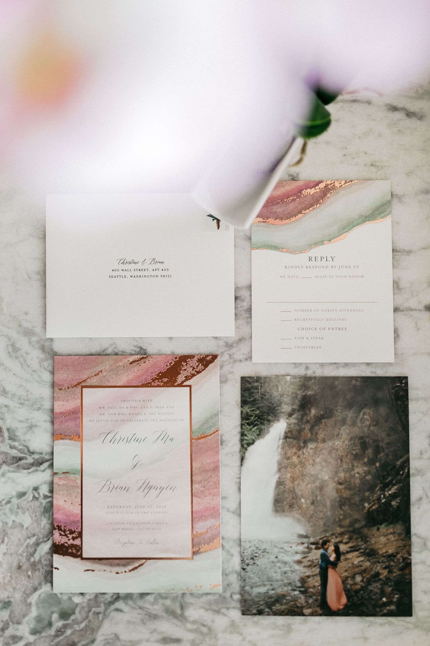Modern wedding invitations featuring marble and pink watercolor designs laid out on a light surface.
