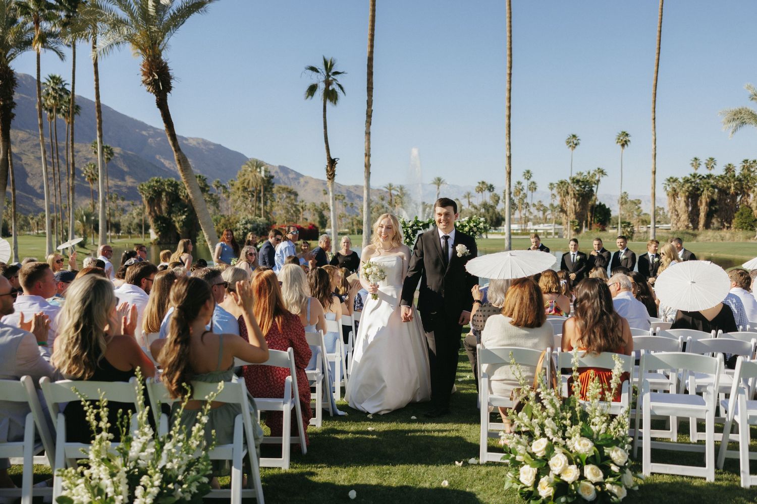 Newlywed couple walks back down the aisle after their outdoor Palm Springs wedding ceremony with mountain views.