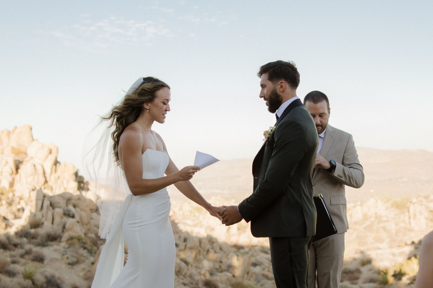 Intimate wedding ceremony taking place at sunset against dramatic desert cliff backdrop.