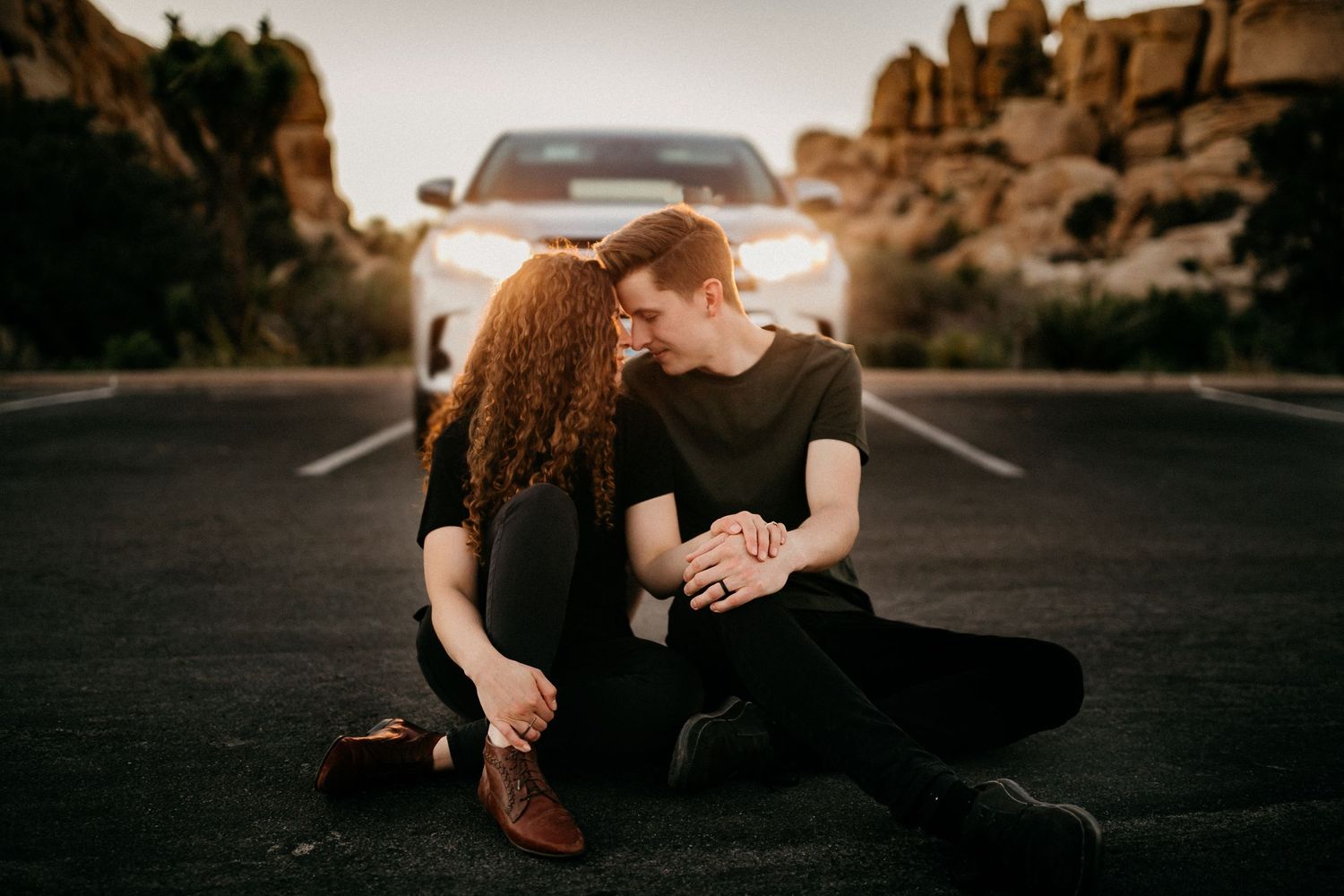 Intimate couple posing on dark ground against desert landscape with large boulders in background.