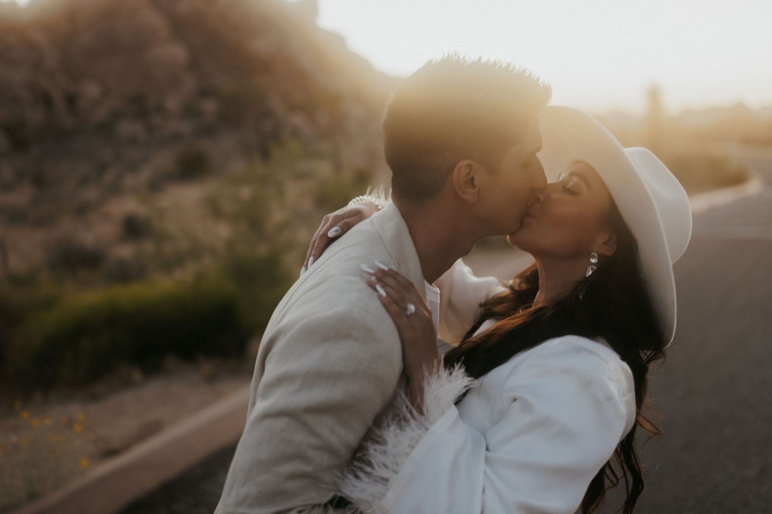 A couple shares a romantic embrace at sunset on a hillside path creating a silhouette against the golden light.