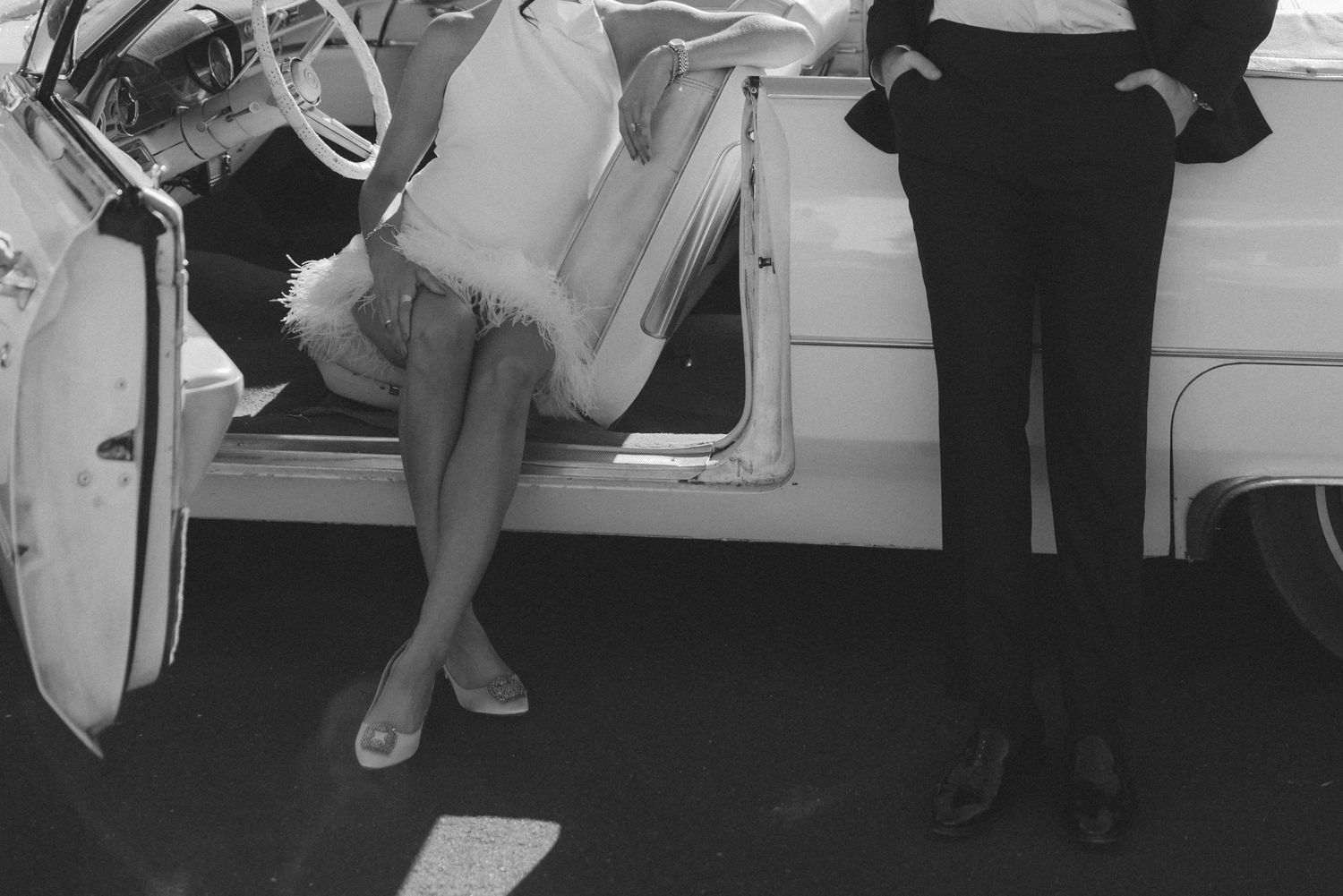Black and white photo of a woman exiting a vintage white car beside a man in a suit.
