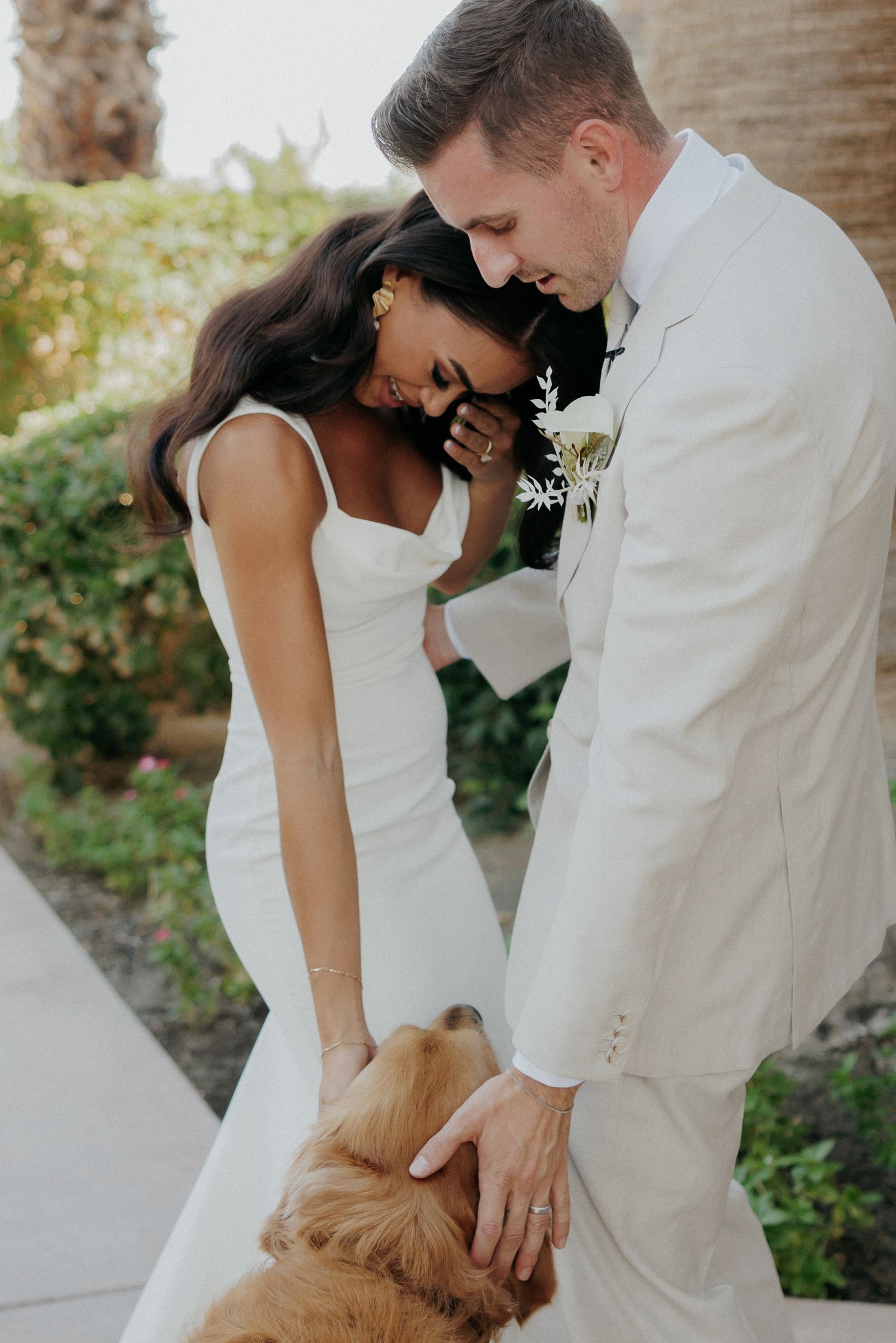 A couple in wedding attire sharing romantic moments with their golden retriever dog outdoors.