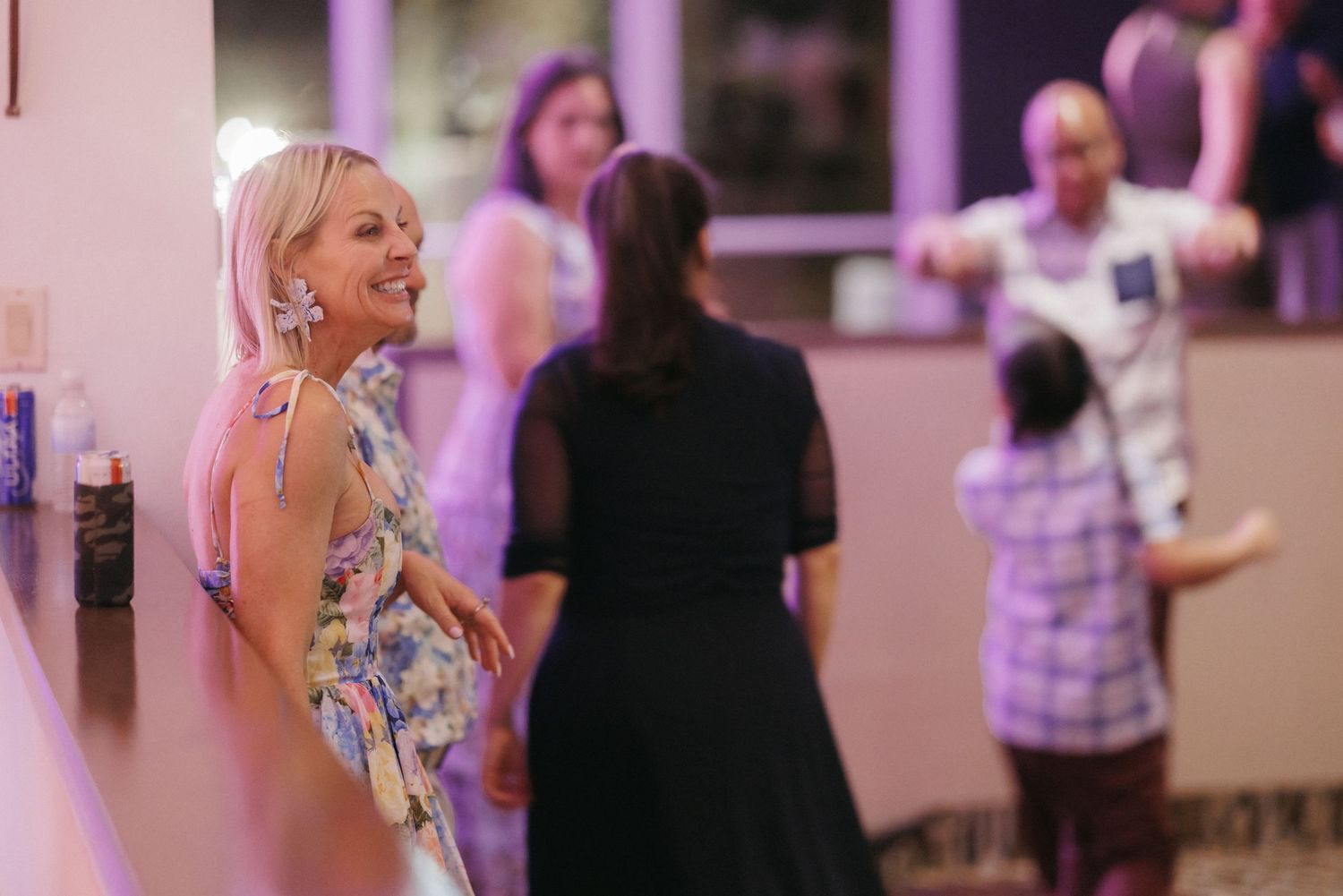 Wedding guest smiling and laughing at lively reception celebration with purple ambient lighting.
