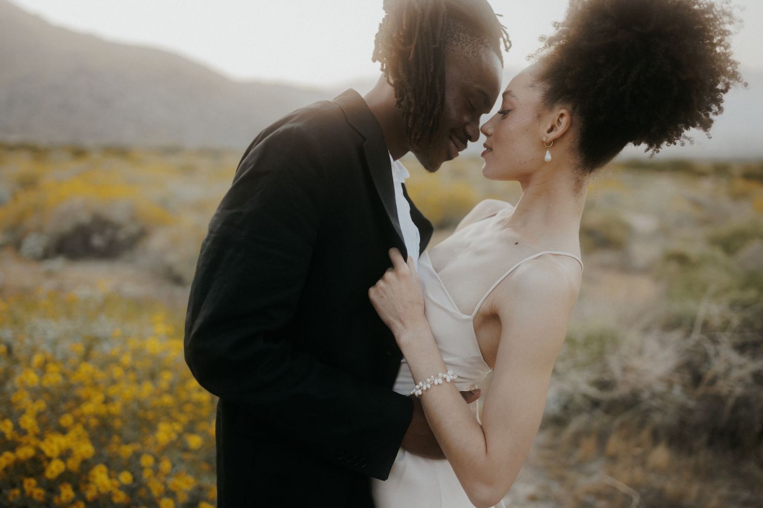 A couple embraces in a field of yellow wildflowers against a moody cloudy sky during a romantic photoshoot.