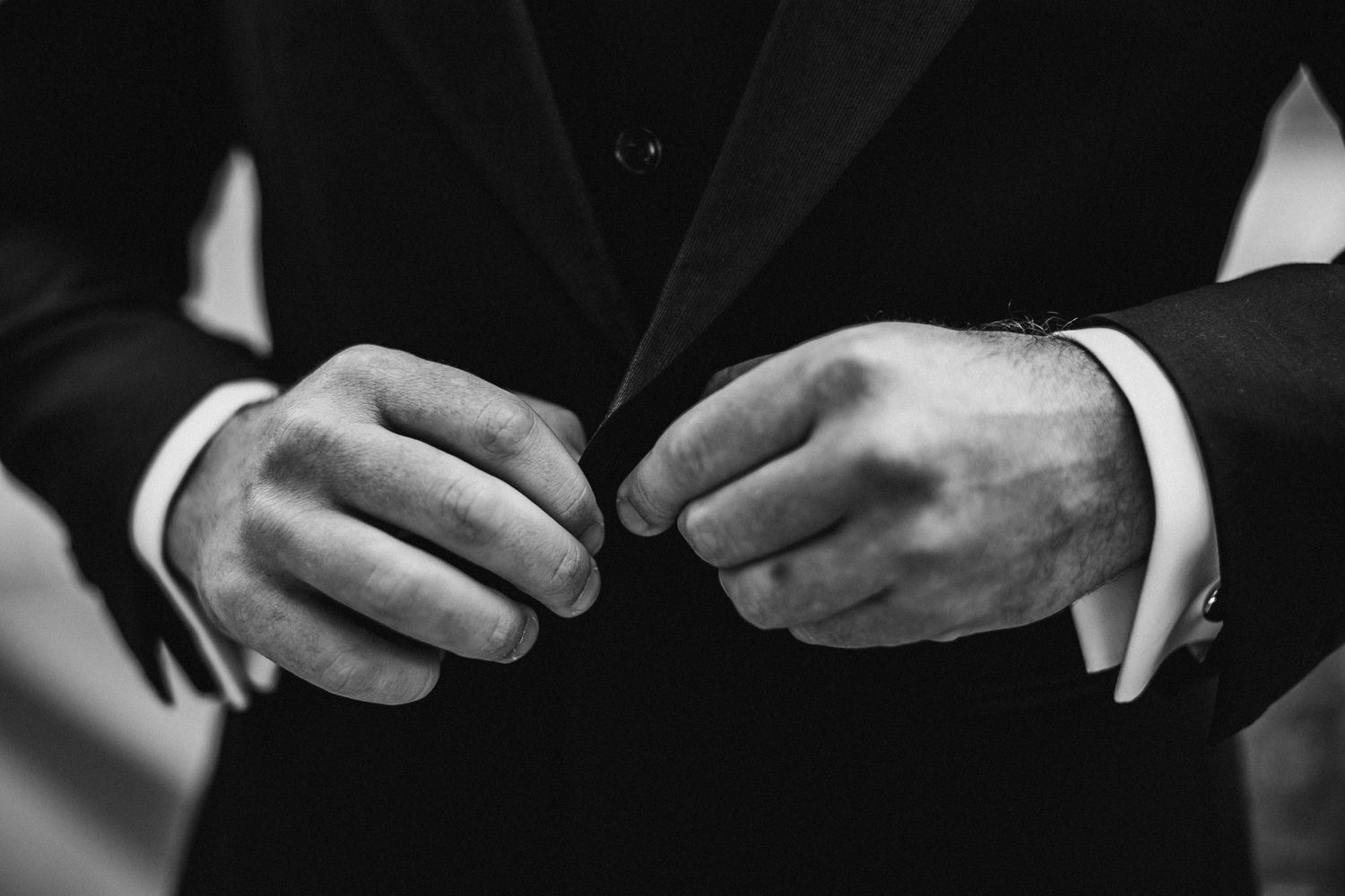 Close-up black and white shot of hands exchanging wedding rings during a ceremony.