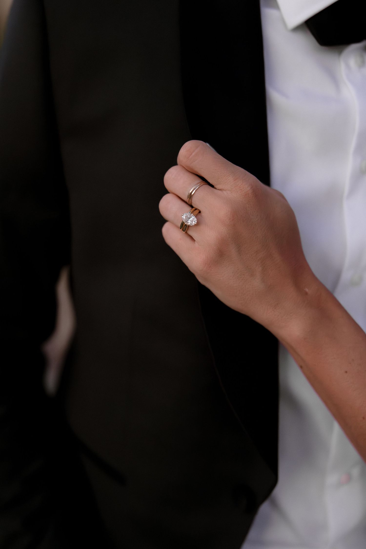 A hand wearing a white sleeve displays a sparkling diamond engagement ring against a dark background.