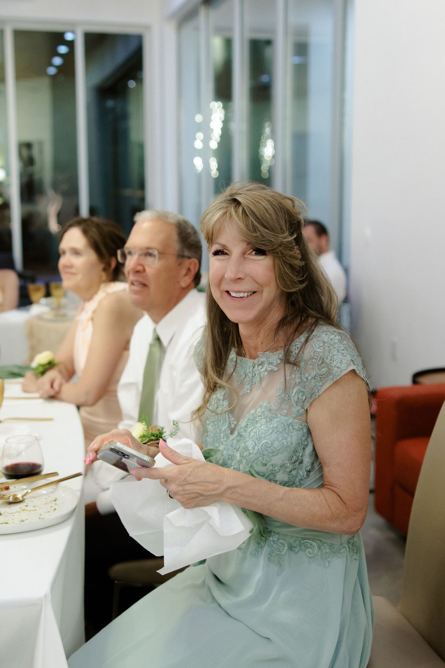 Joyful guests dressed in formal attire share laughter and conversation during an elegant reception dinner at an indoor venue.