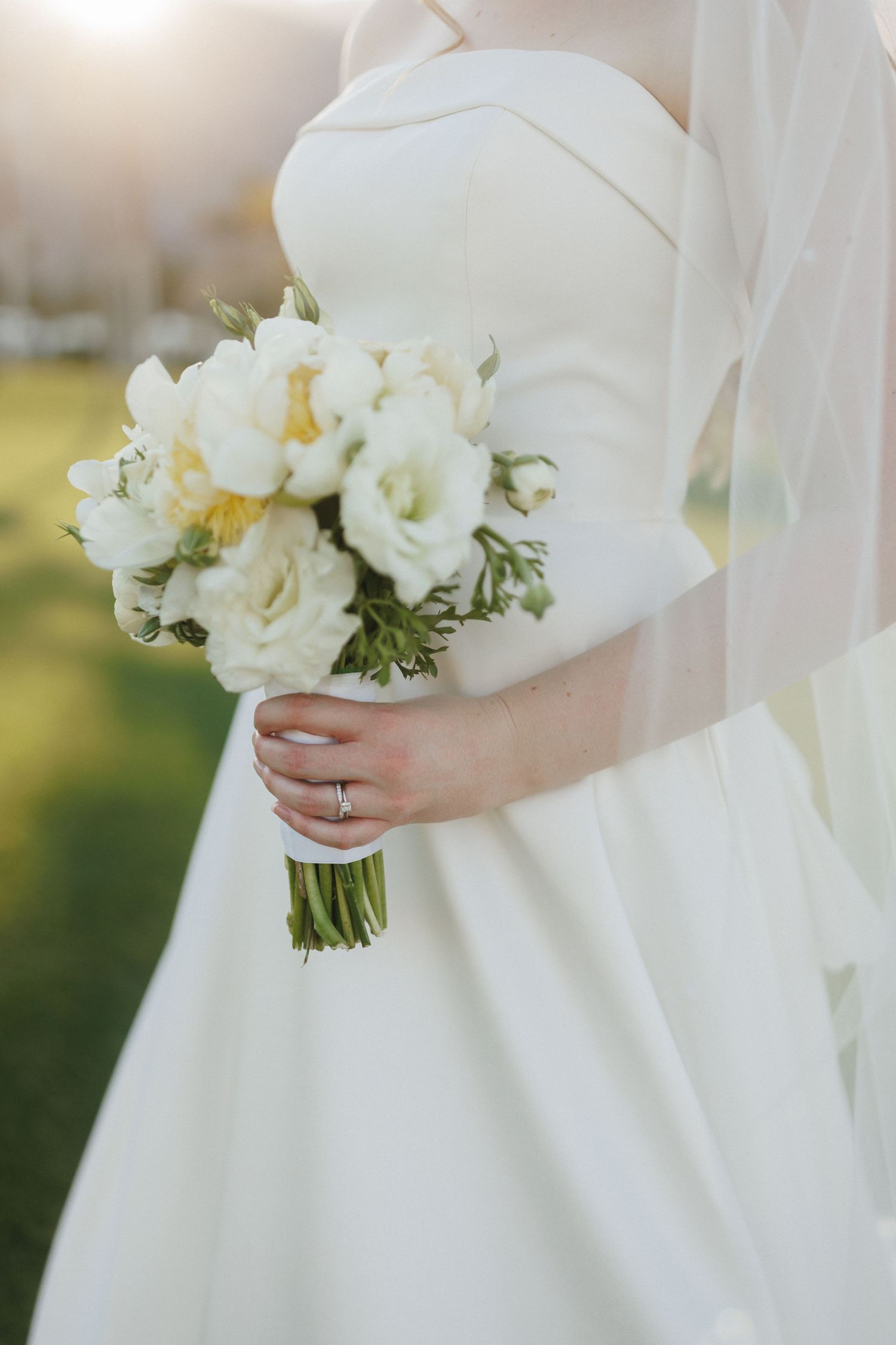Bride in strapless white gown holding elegant white peony and rose bouquet with veil.
