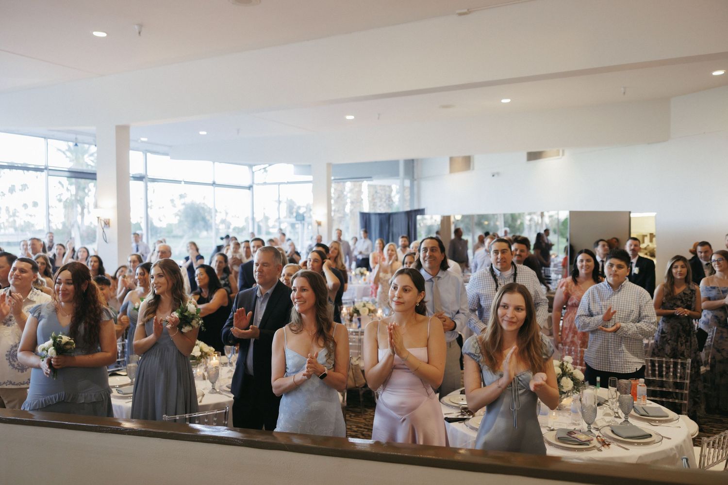 Wedding guests clapping and celebrating as the bride and groom enter the modern reception venue.