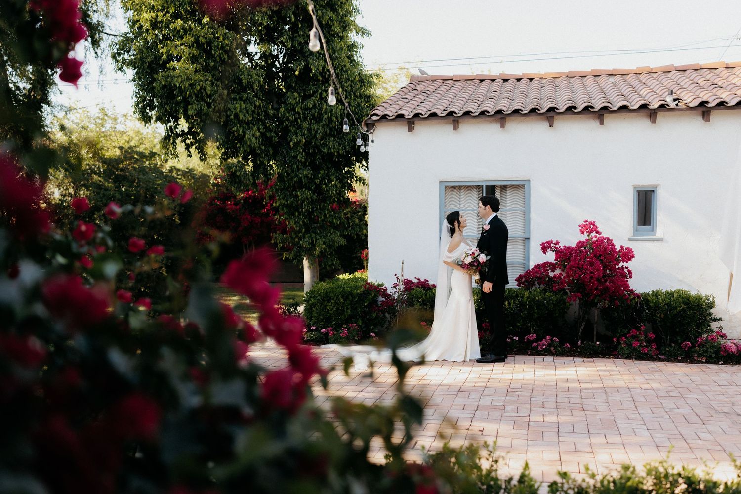 Mediterranean style wedding venue with white stucco walls and vibrant red bougainvillea flowers blooming in a garden setting.