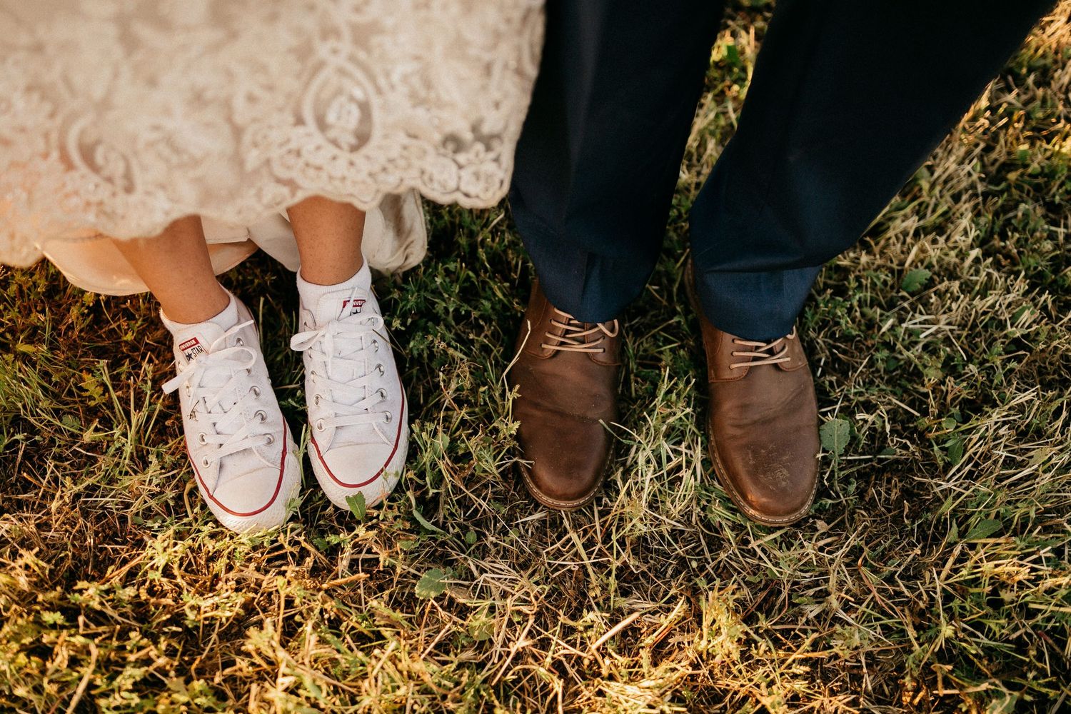 A row of feet wearing different types of shoes standing in a grassy field at sunset.