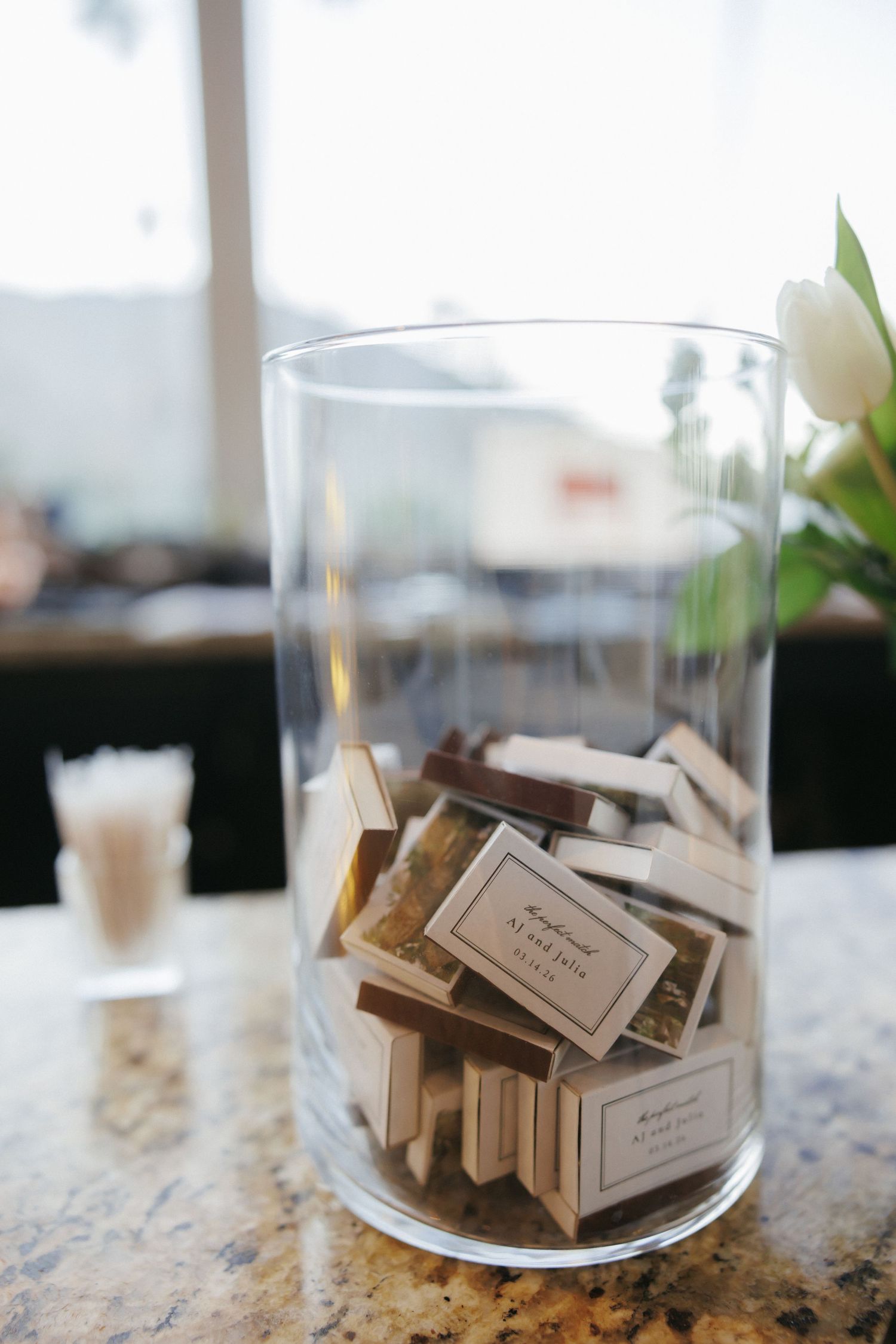 Glass vase filled with personalized matchbook wedding favors displayed on reception table.