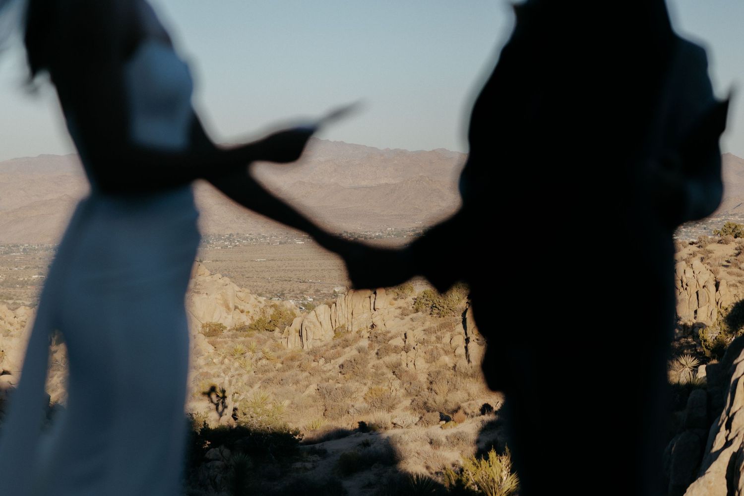 Silhouetted group of people standing against a bright sunset sky with mountains in the background.