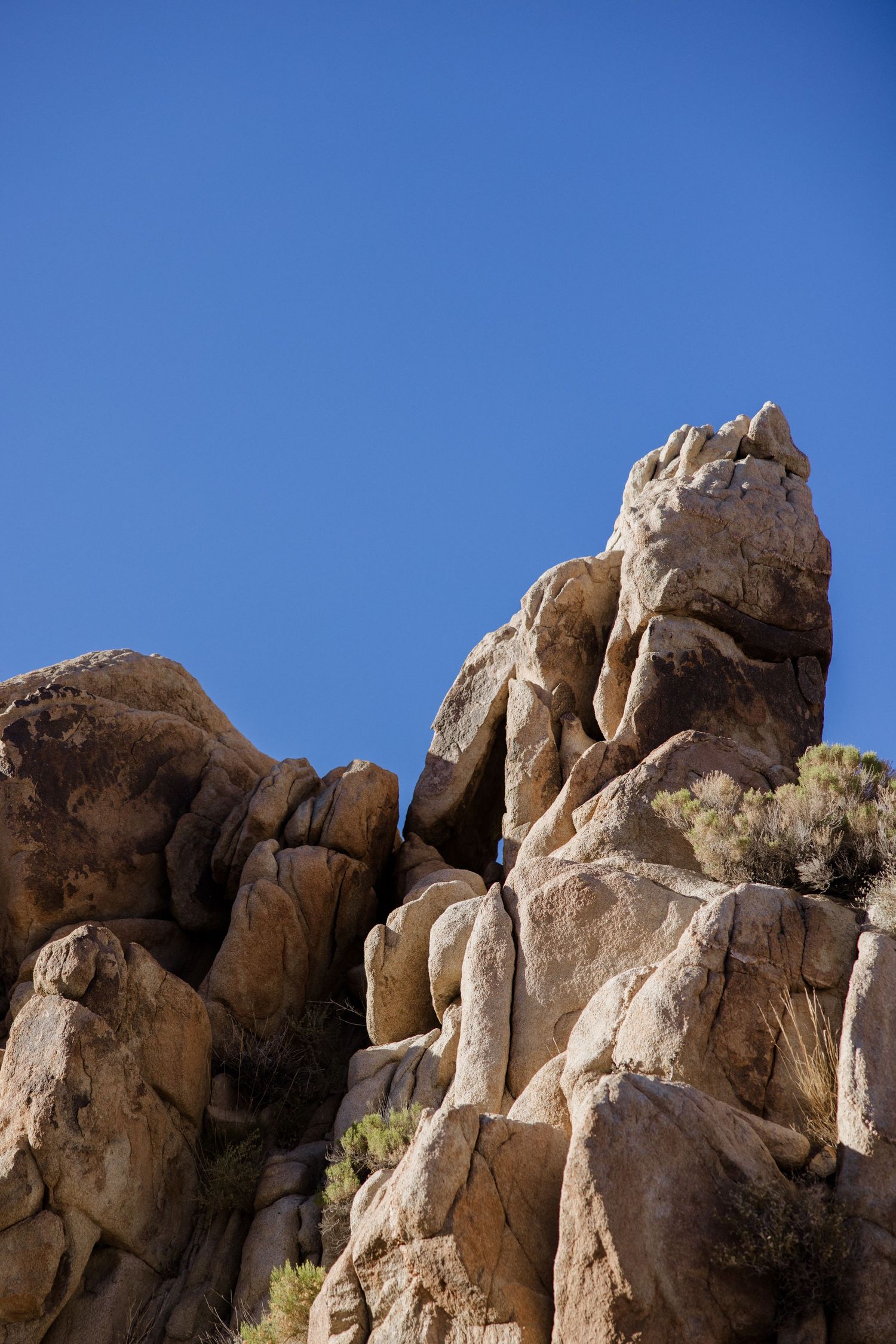 Rugged granite rock formations tower against a bright blue sky in a desert landscape.