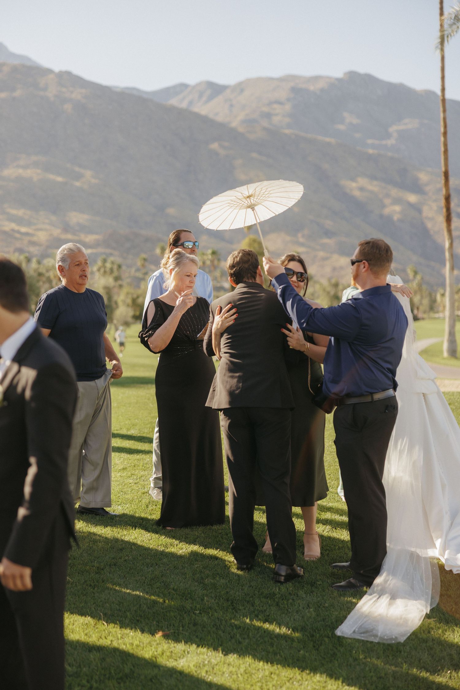 Wedding guests greeting bride outdoors with mountains and palm trees in background.