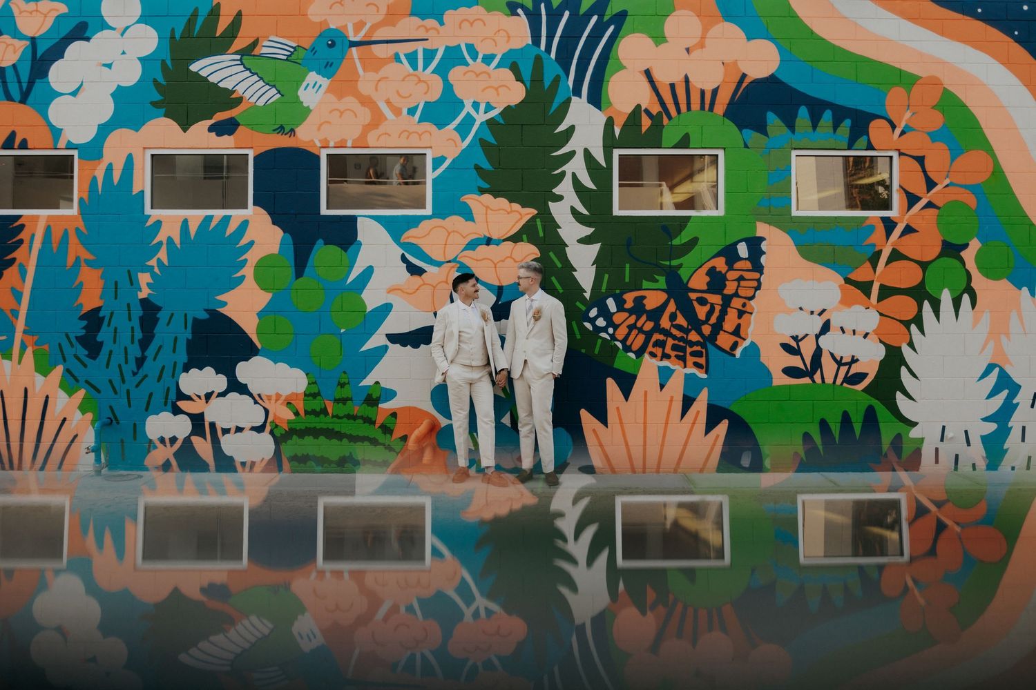 Colorful jungle-themed mural with tropical plants and silhouetted figures painted on a brick wall.