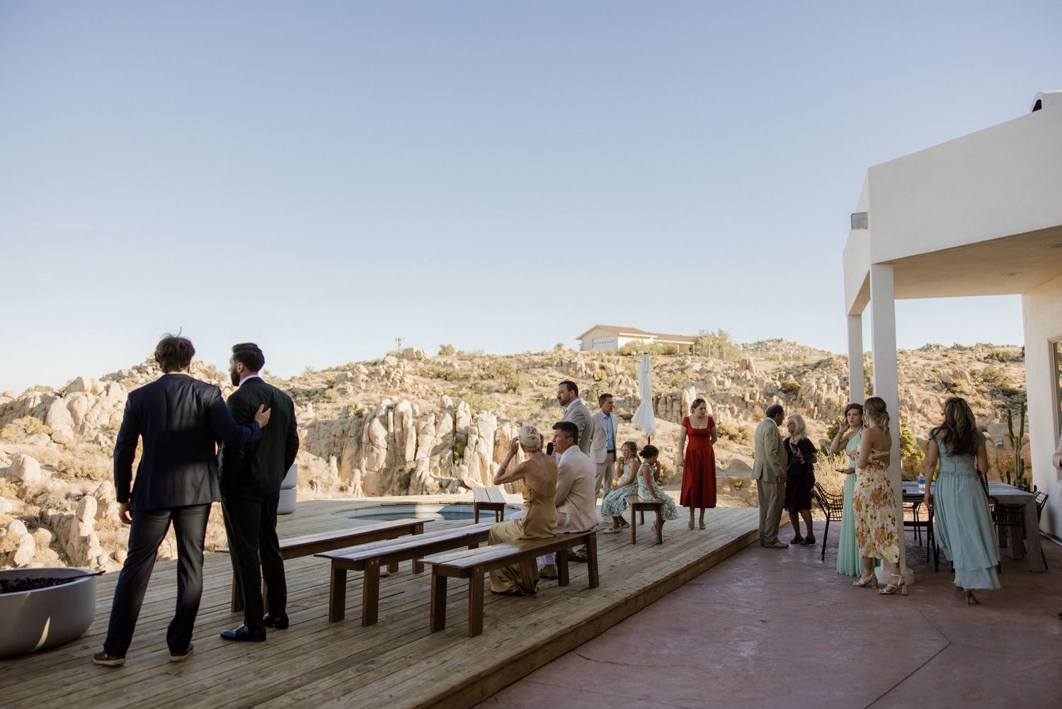 Wedding guests gather on a terrace overlooking scenic rocky cliffs and mountains during an outdoor celebration.