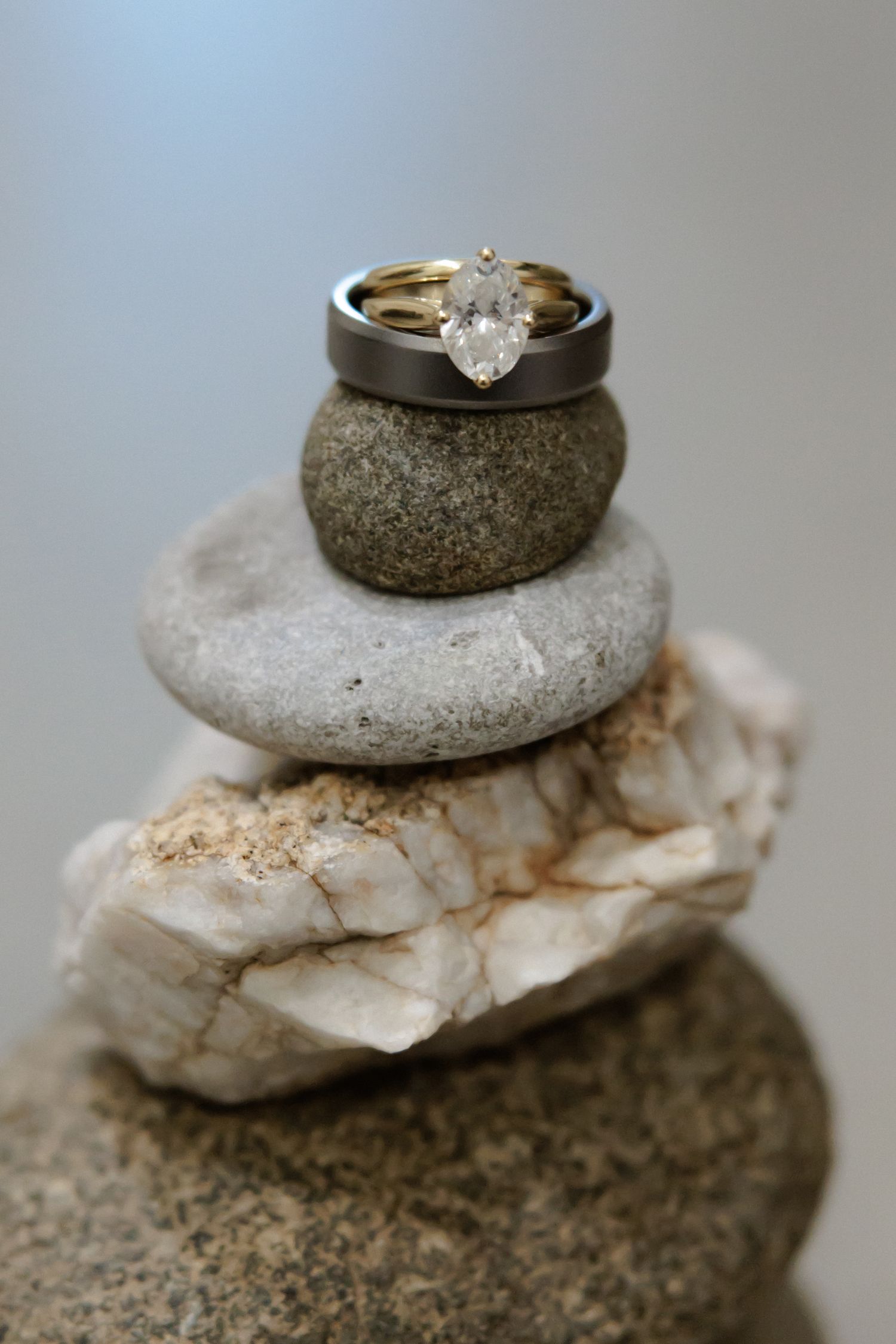 Wedding rings displayed on artfully stacked natural stones against a neutral gray background.
