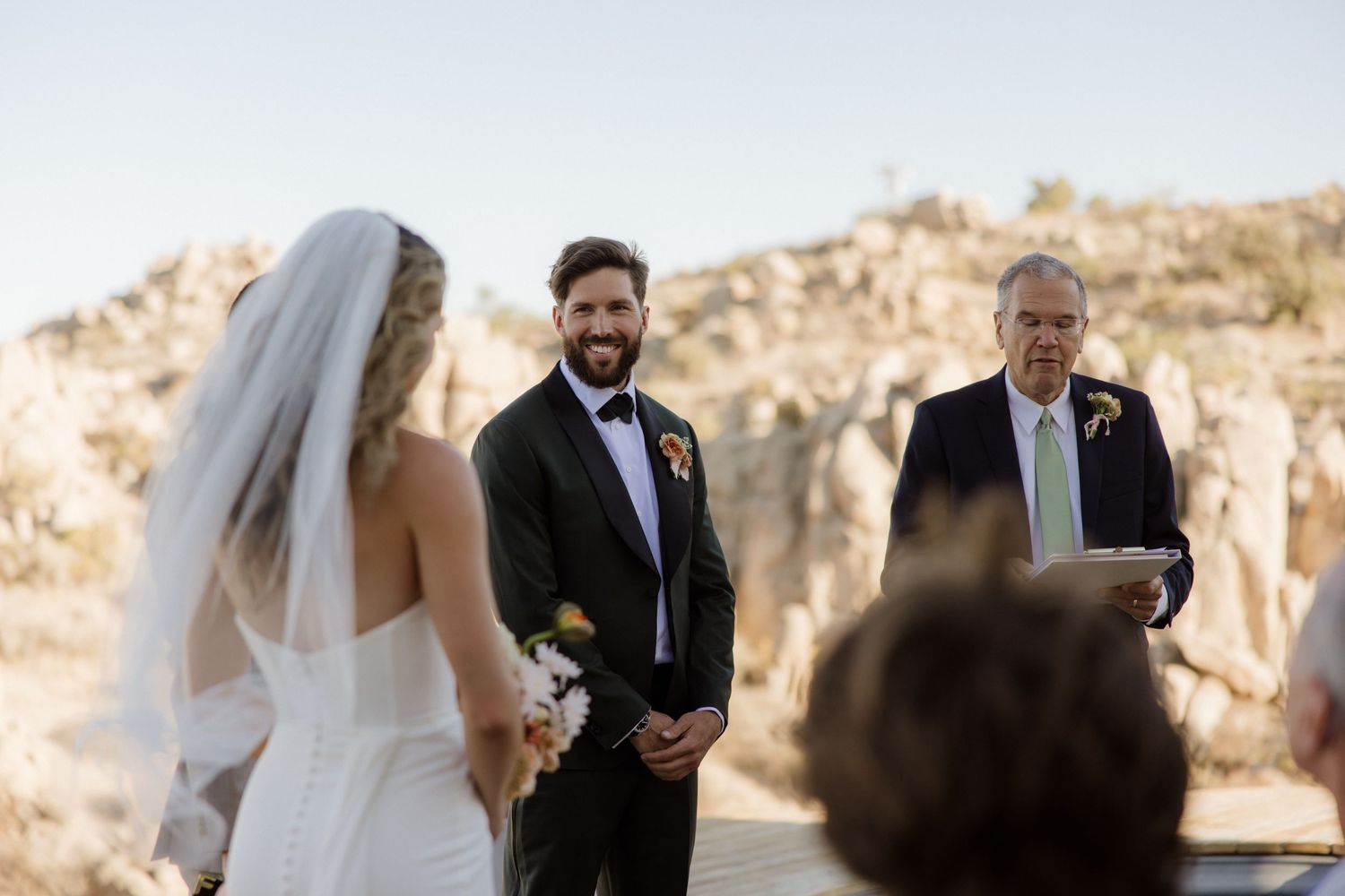 Wedding ceremony taking place against dramatic desert rock formations in an outdoor setting at sunset.