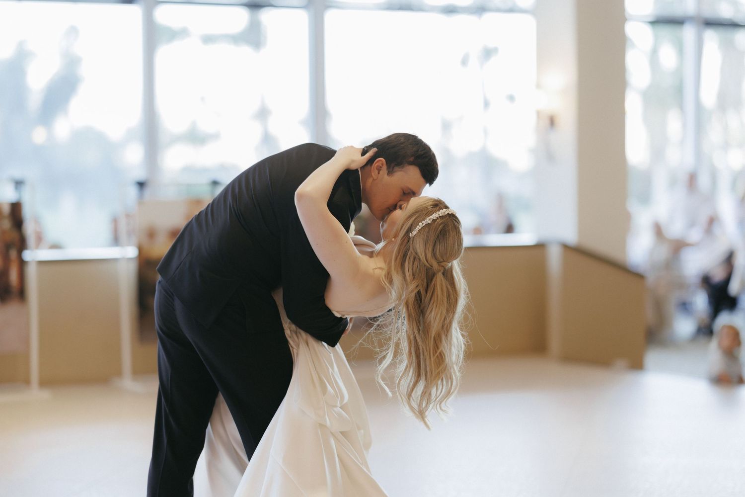 Groom dips bride in a romantic first dance at elegant wedding reception with warm natural lighting.