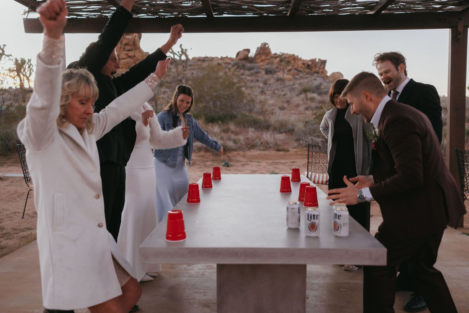 Wedding guests celebrate playing beer pong with red cups at outdoor desert reception.