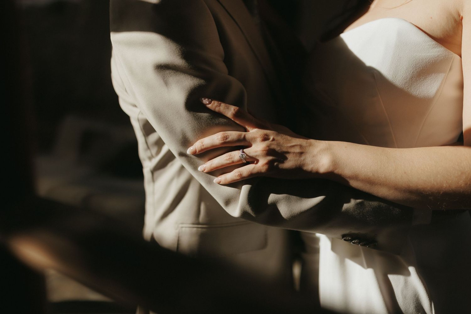 Close-up of a couple holding hands, bride in white dress and groom in gray suit, in warm golden light.