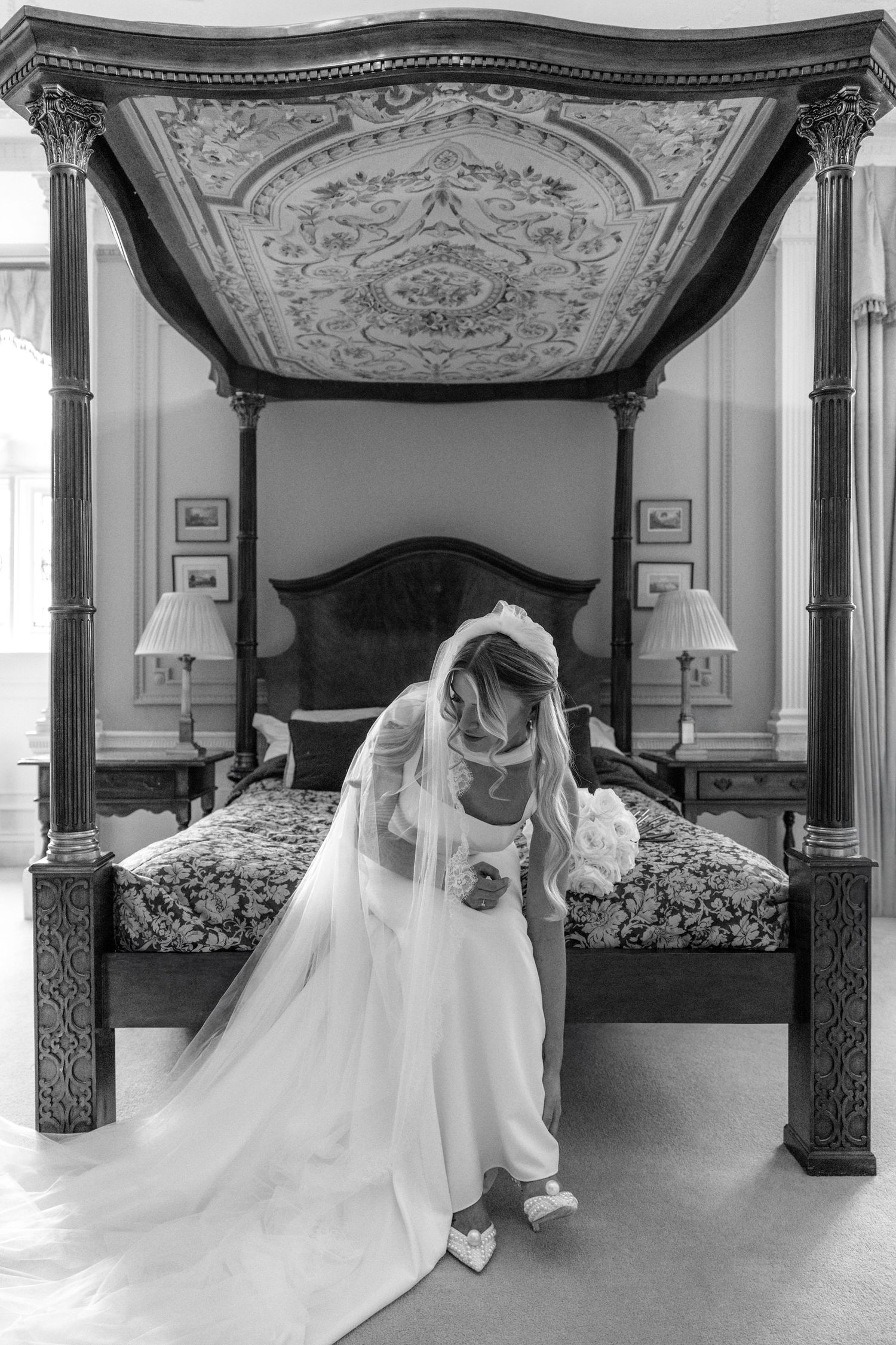 Black and white photo of bridal gown and veil against ornate canopy bed.