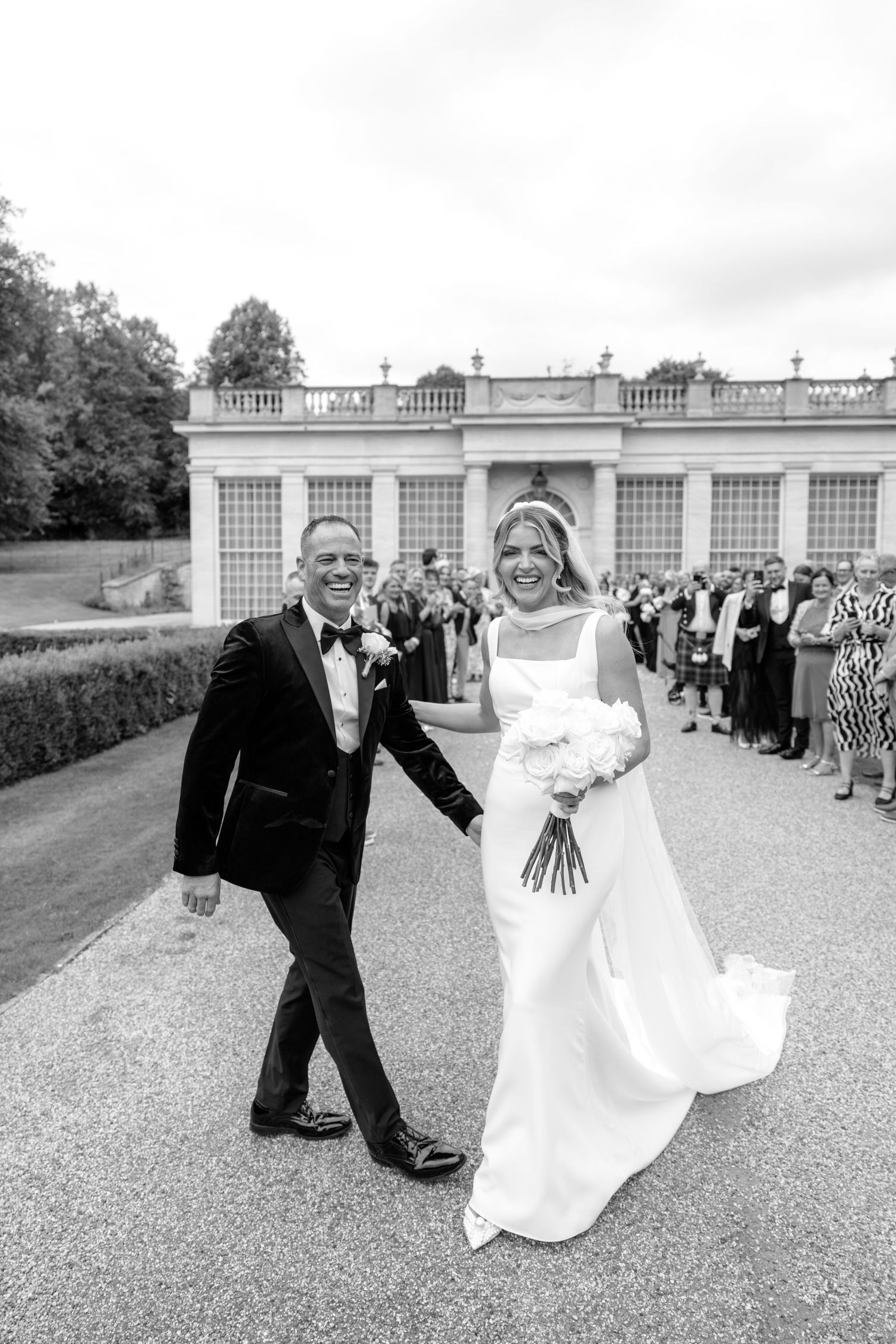 Happy couple walking down path after wedding ceremony at elegant mansion.