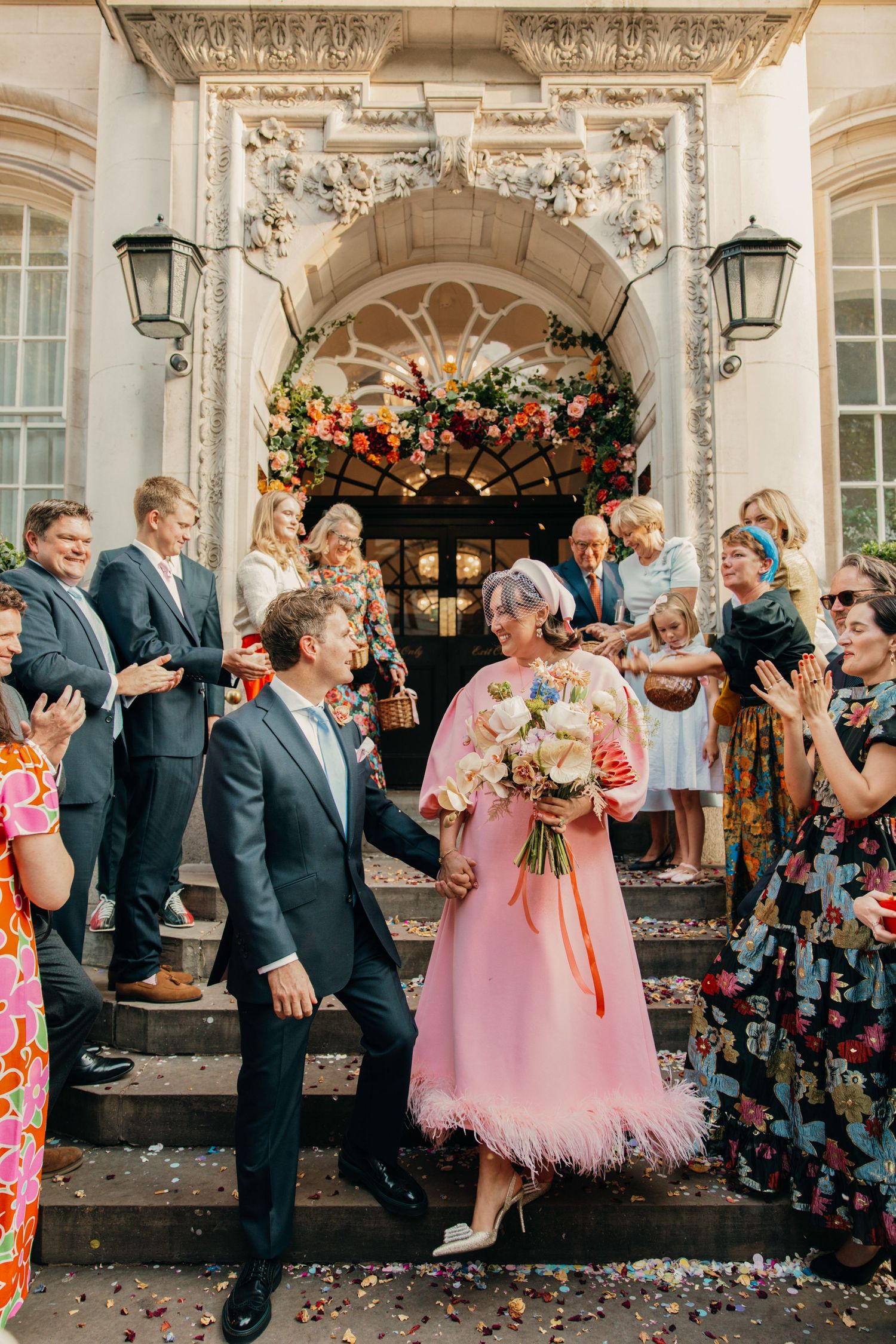 Wedding celebration on ornate building steps with guests cheering and floral decor.