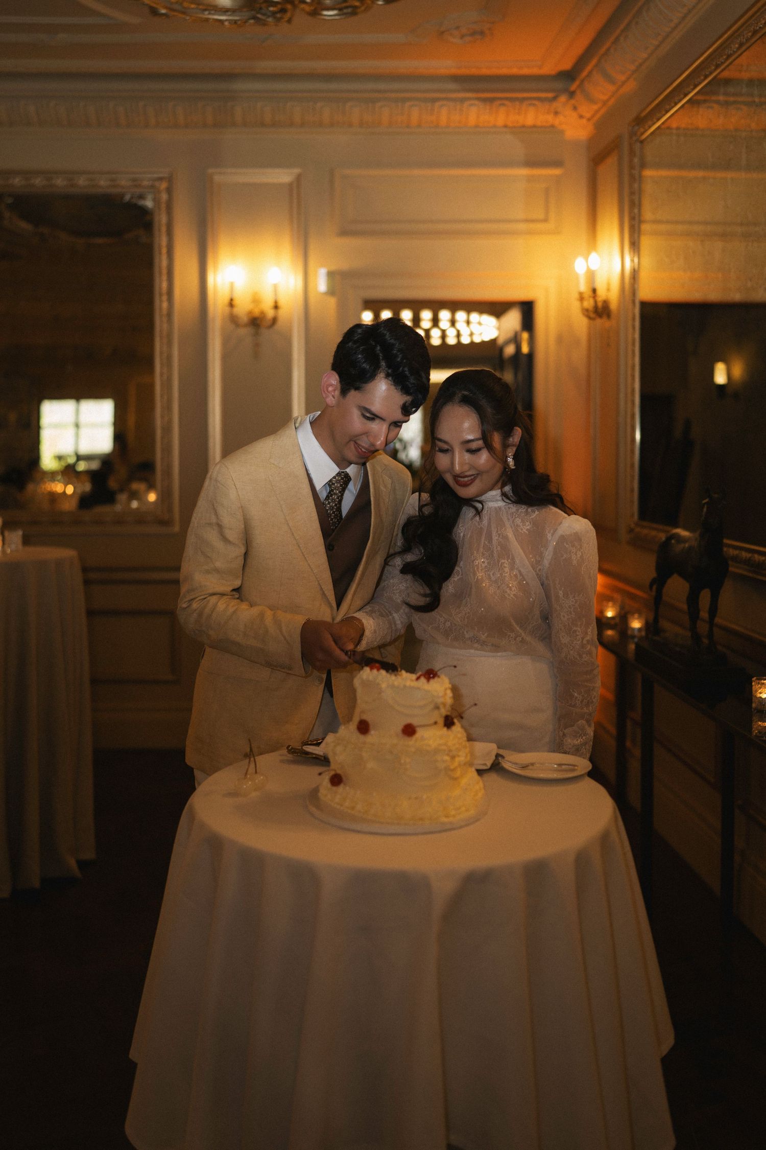 Bride and groom cutting a white wedding cake together in an elegantly lit reception venue.