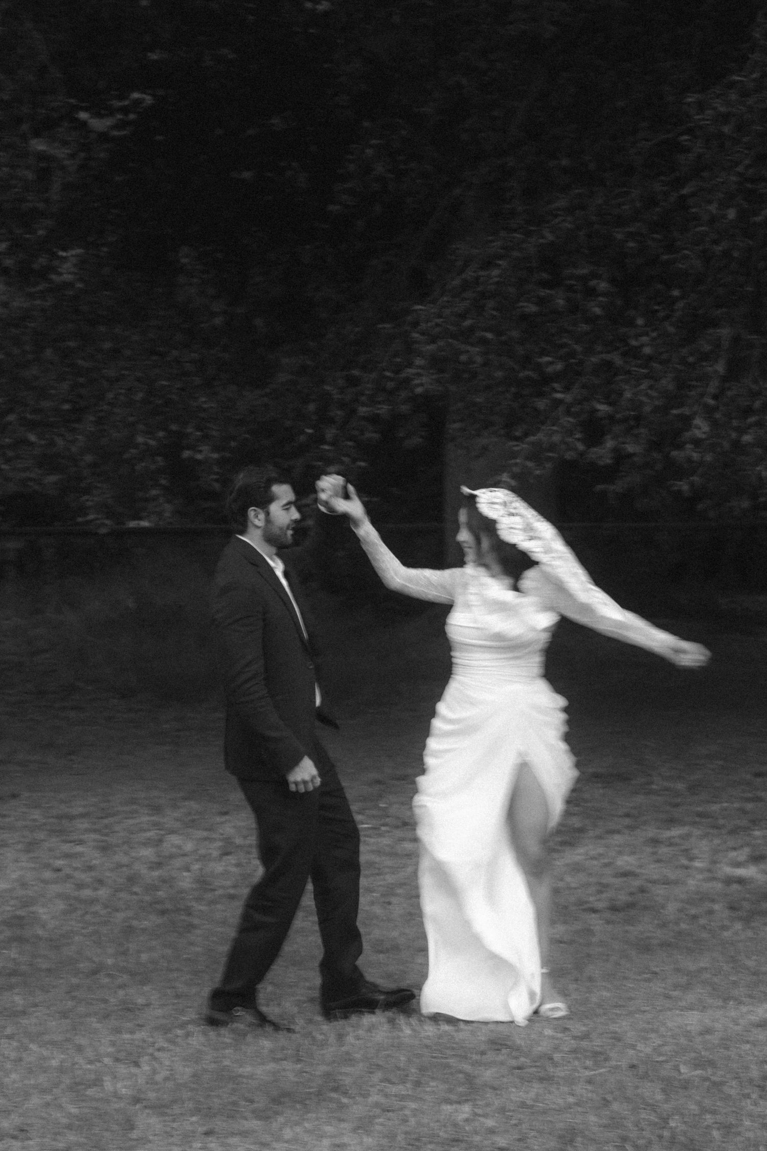 Black and white photo of a bride and groom dancing outdoors, with her veil flowing as he spins her.
