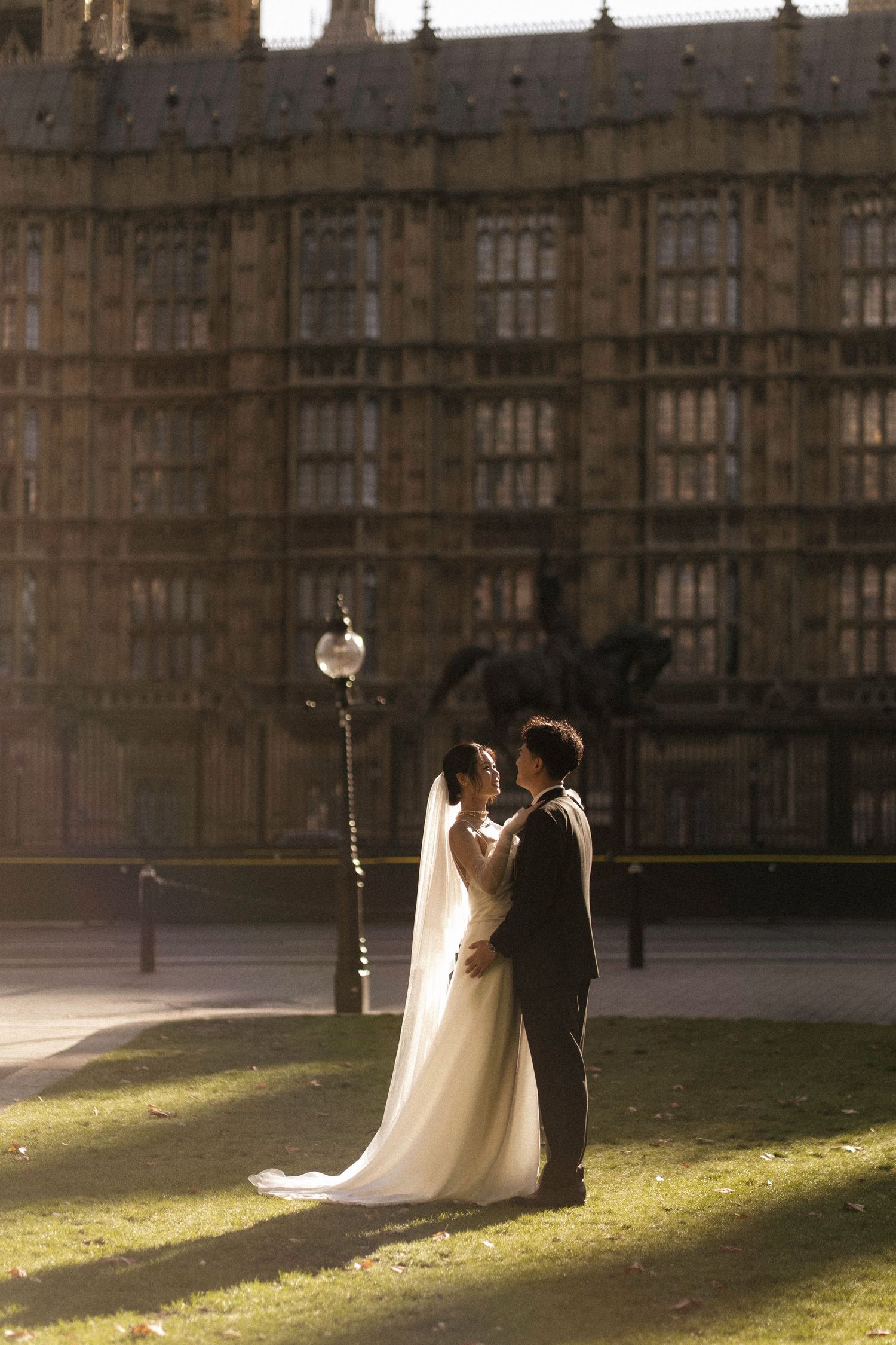 Bride and groom embrace in golden sunlight before the Houses of Parliament, London, in an elegant wedding portrait.
