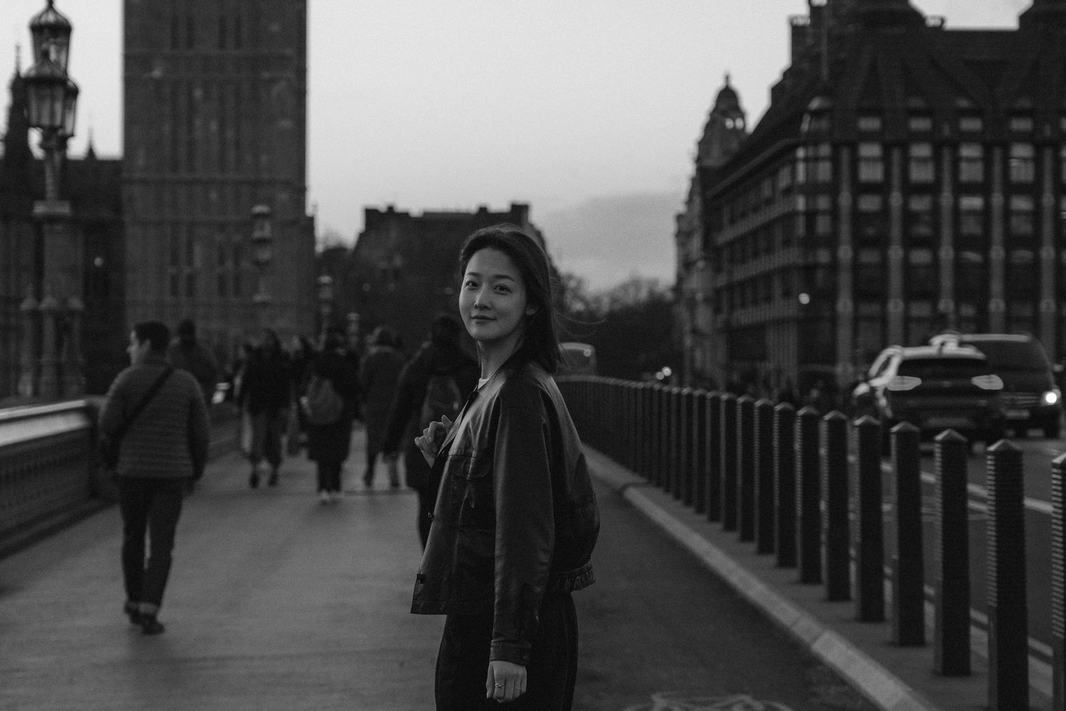 Person walking across a bridge in black and white with urban architecture in the background.