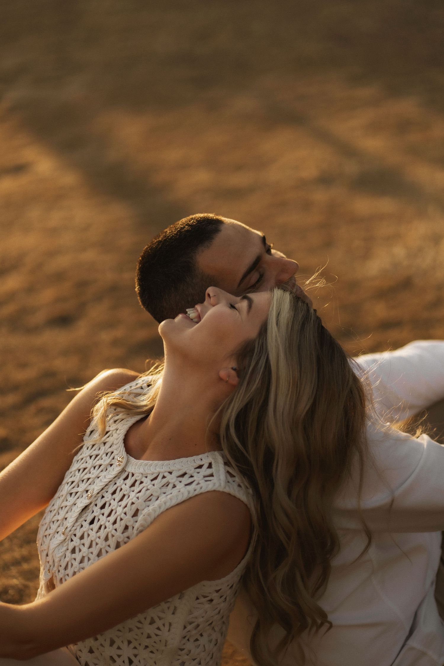 A couple in white clothing lying together on brown ground at sunset with warm golden light.