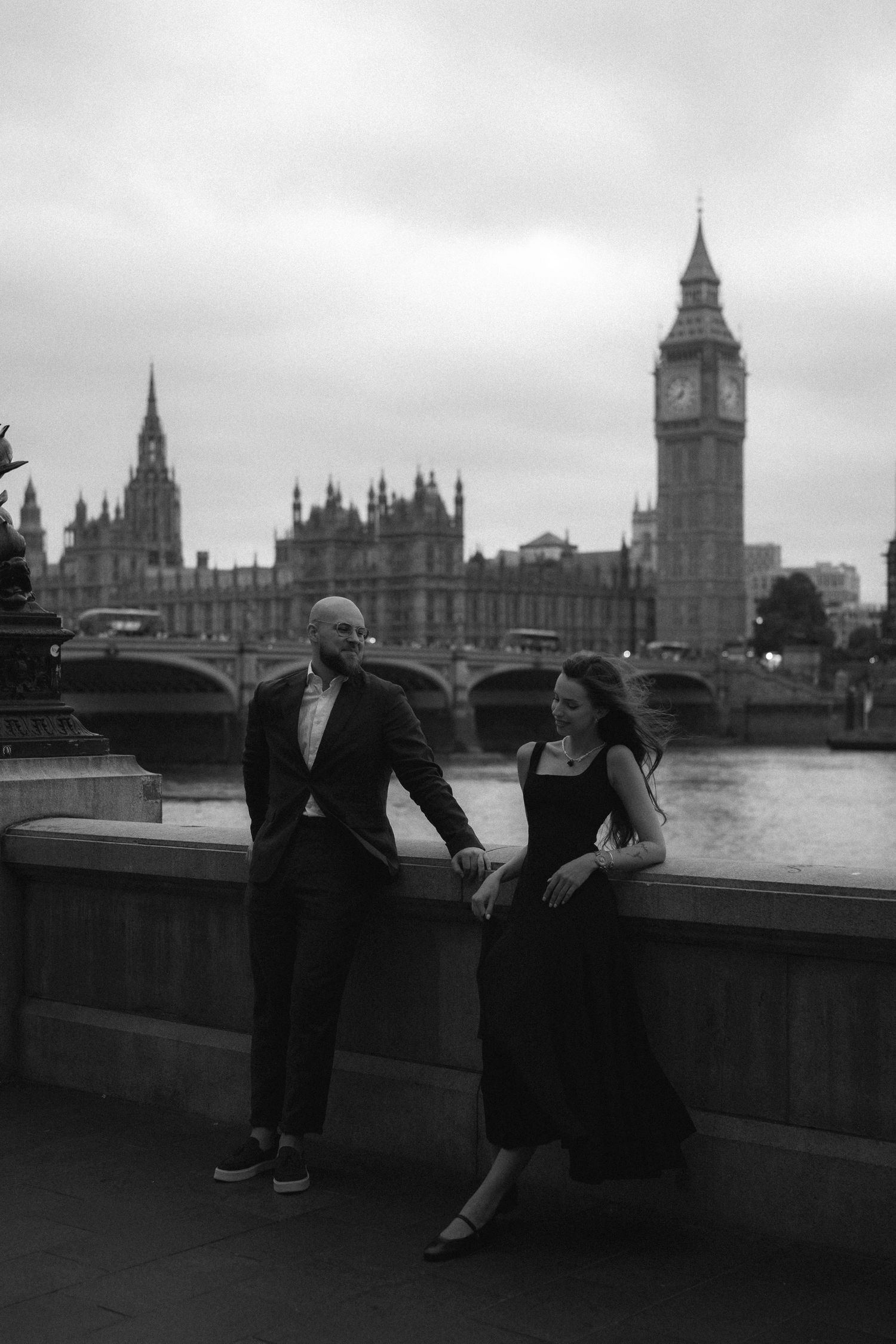 Black and white series of photos showing people sitting and conversing on a wall overlooking the Thames with Big Ben in view.