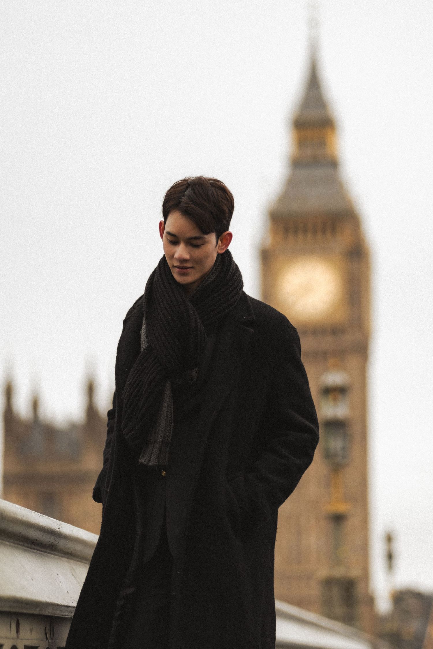 Person in black coat and scarf stands against London cityscape with Big Ben tower visible in background.