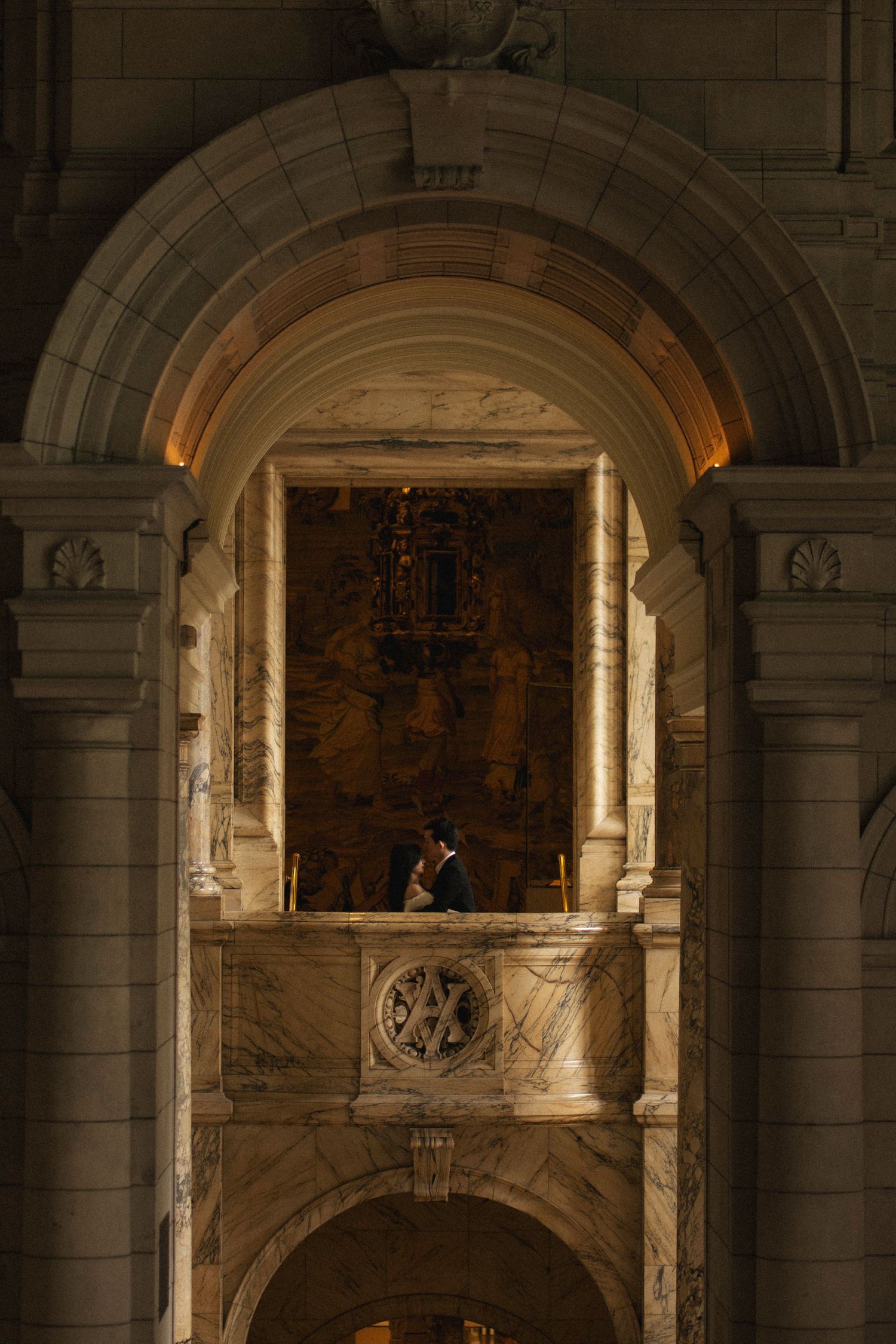 A violinist performs in a historic stone archway with dramatic lighting illuminating the classical architectural details.