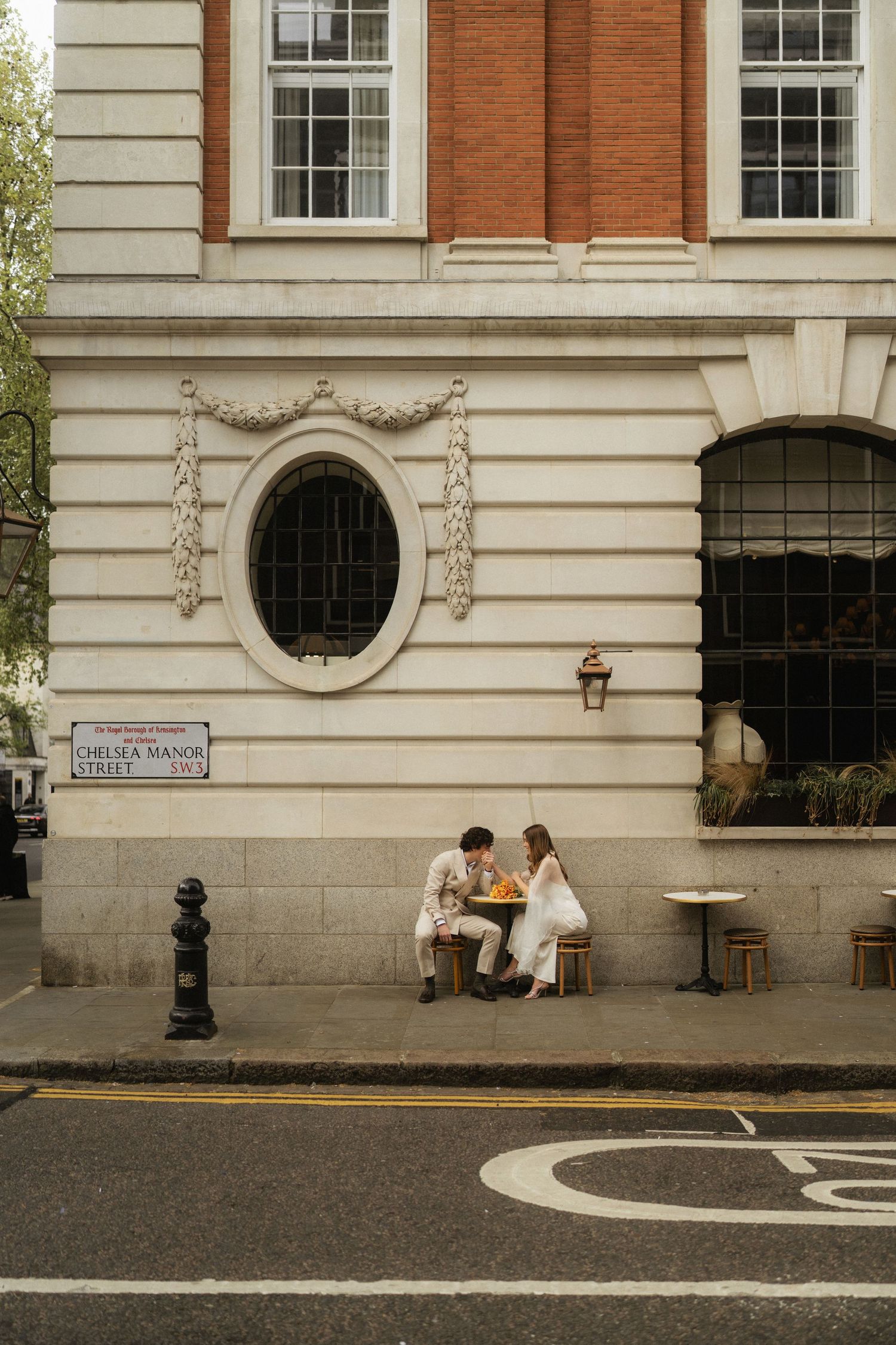 Couple sitting outside a classic London building on Chelsea Manor Street, sharing a romantic moment on a quiet street.