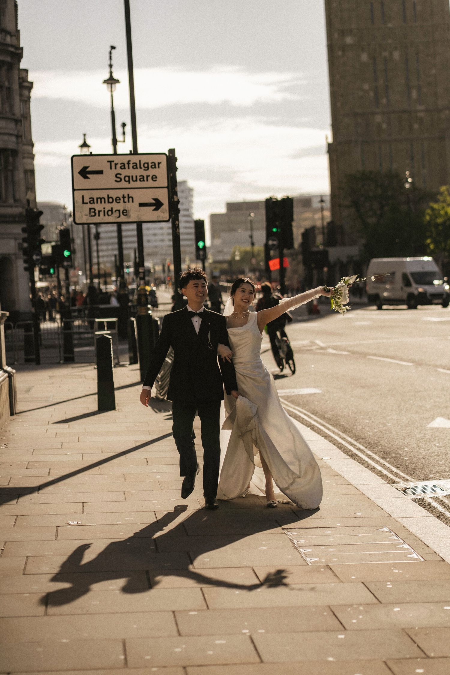 Bride and groom walking near Trafalgar Square sign in London, bride in white gown with arm outstretched.
