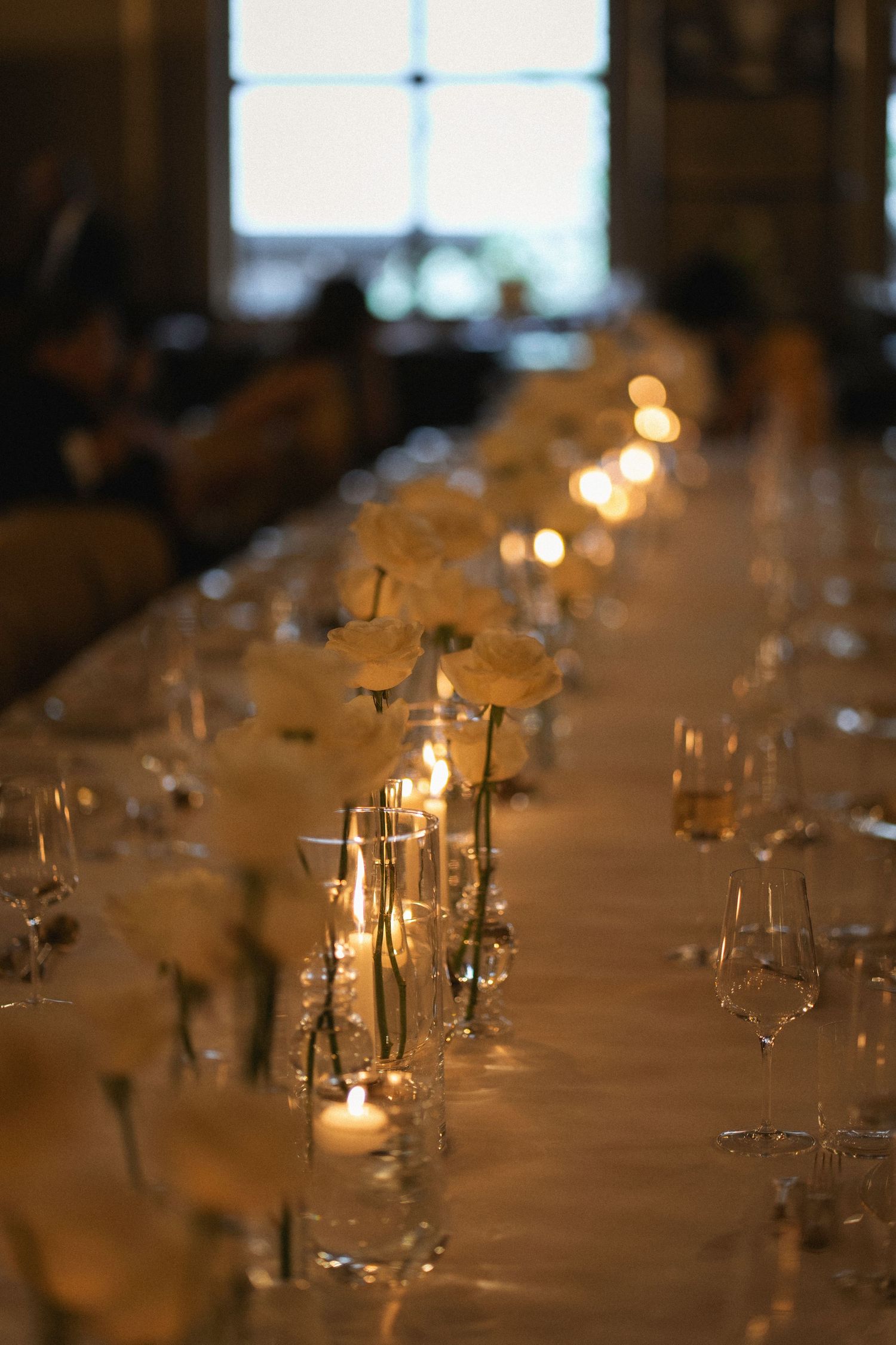 Elegant wedding table setting with white roses and glowing candles in glass vessels creating romantic ambiance.