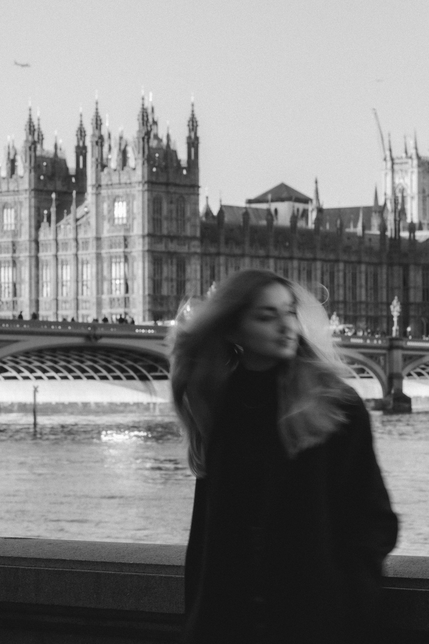 A blurred black and white motion sequence shows a person's hair blowing in the wind near London's Houses of Parliament.
